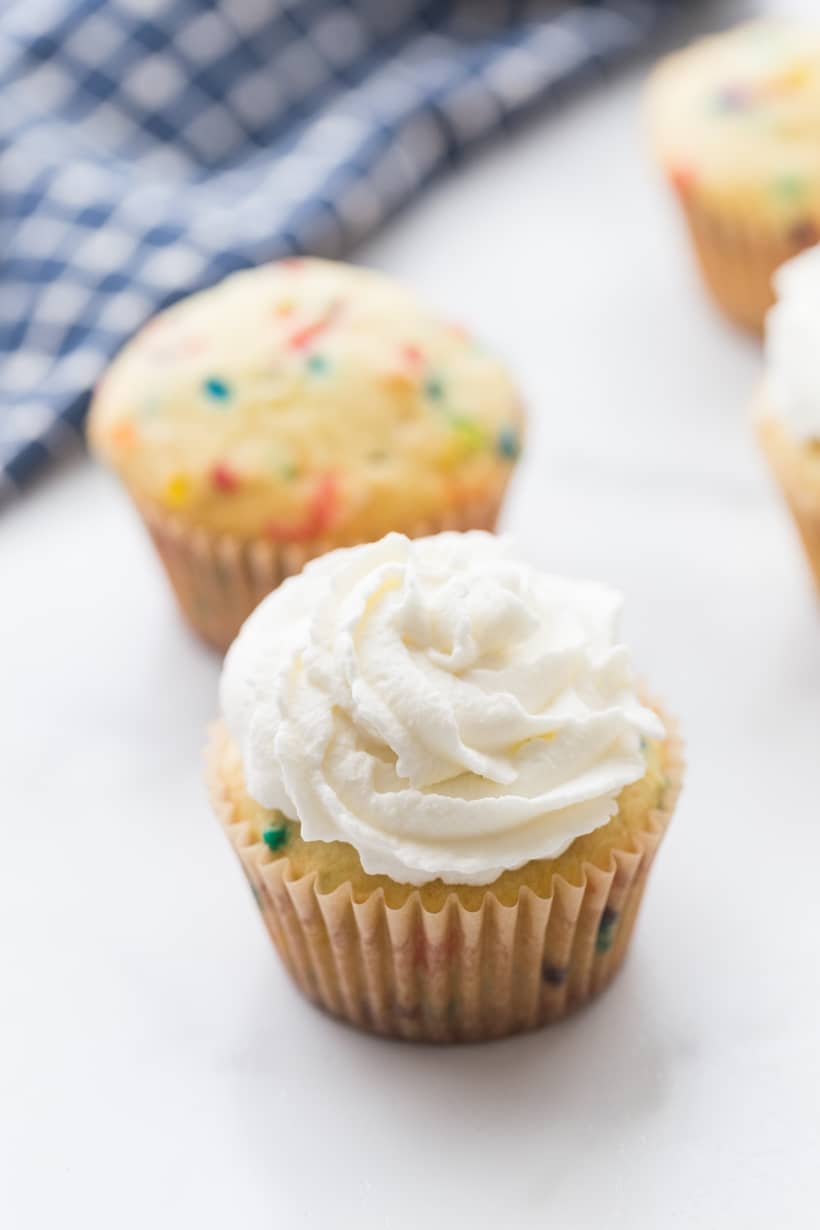 Topping a firecracker cupcake with whipped cream before adding Pop Rocks. Whipped cream topped patriotic cupcake ready for fresh berries and crackling candy.