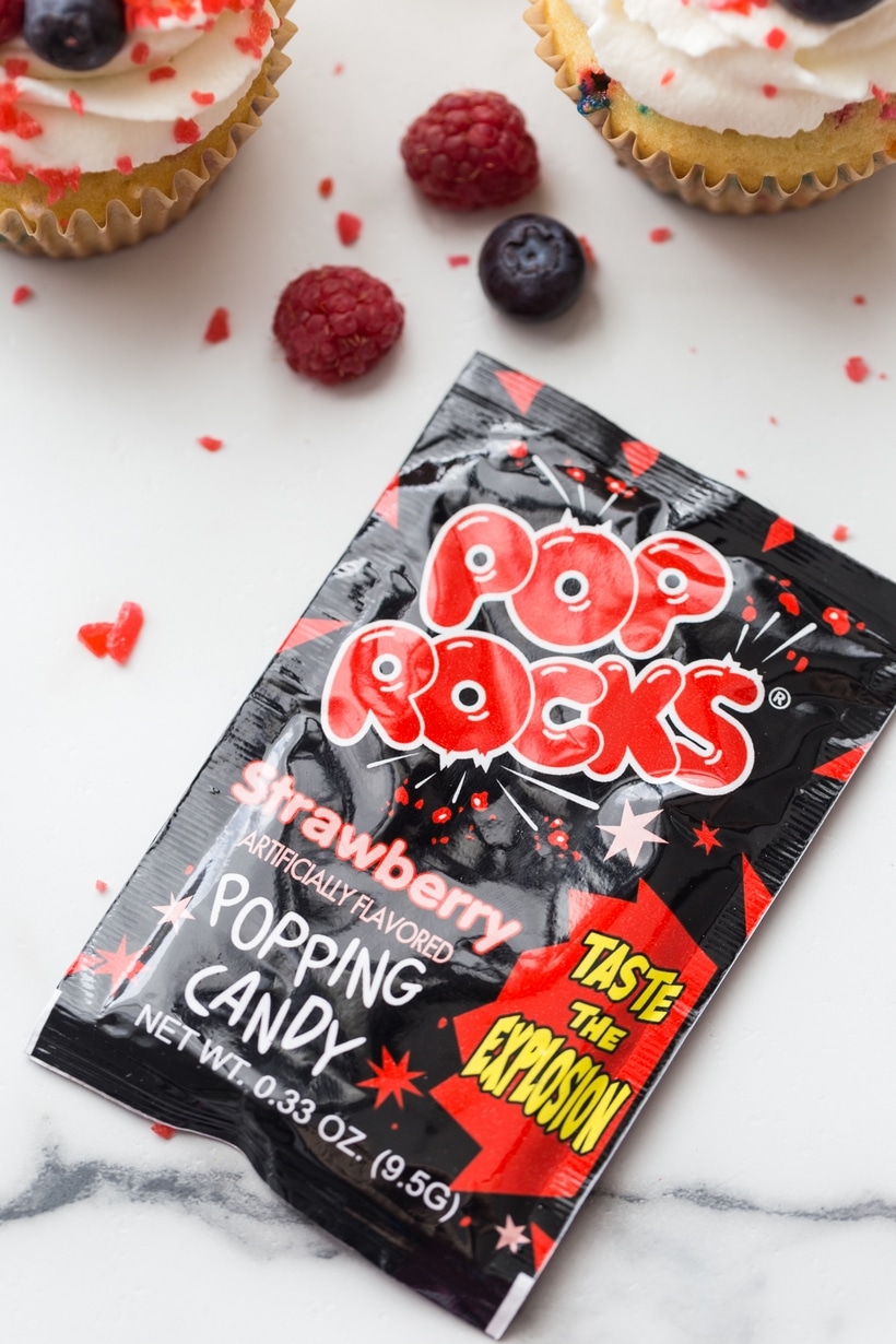 Candy packet next to pop rocks cupcakes decorated with berries. Pop Rocks and 4th of July cupcakes topped with whipped cream and fresh fruit.