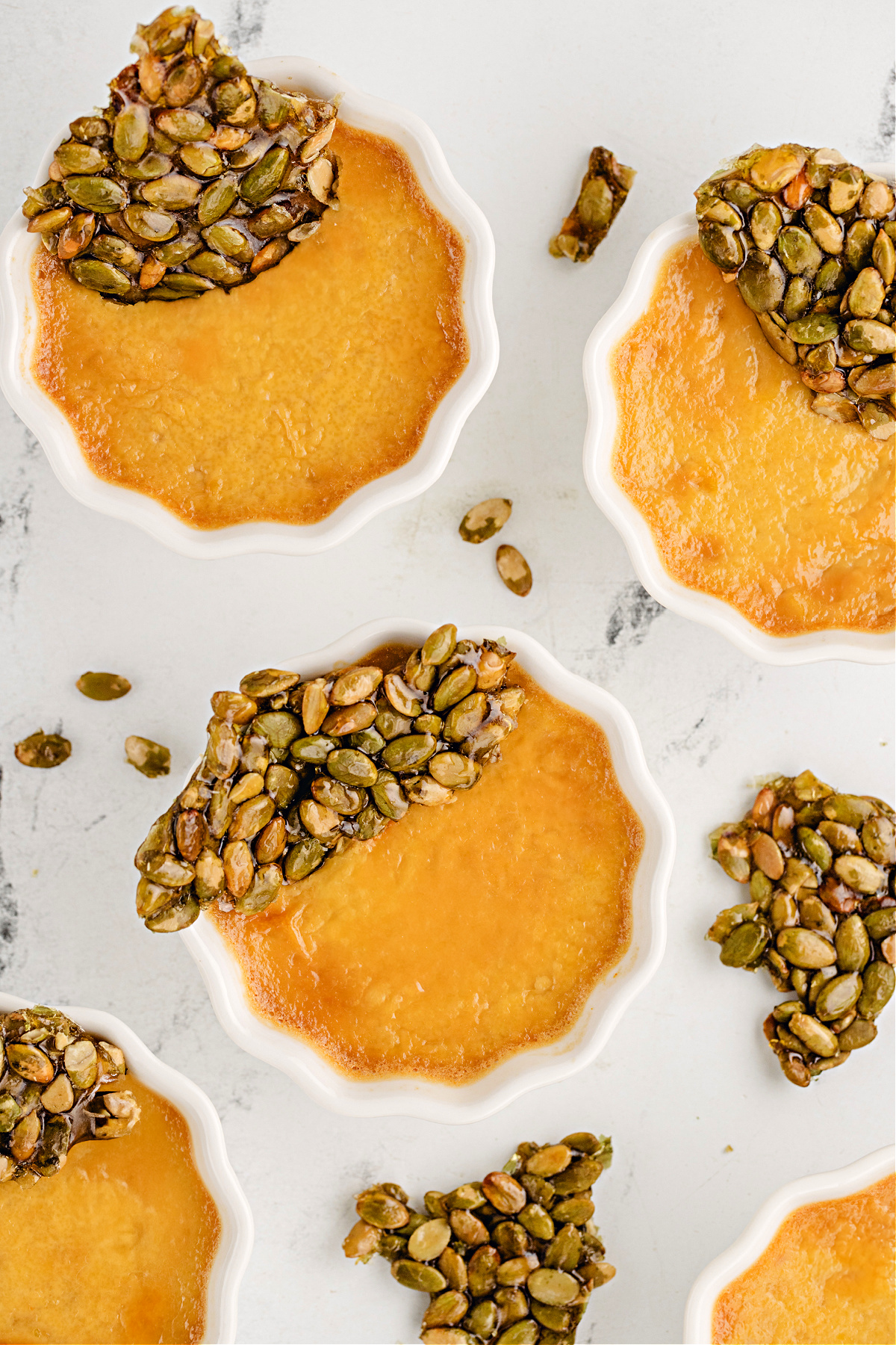 Pumpkin chai custards set in scalloped ramekins with shards of pumpkin seed brittle for texture and fall spice contrast.