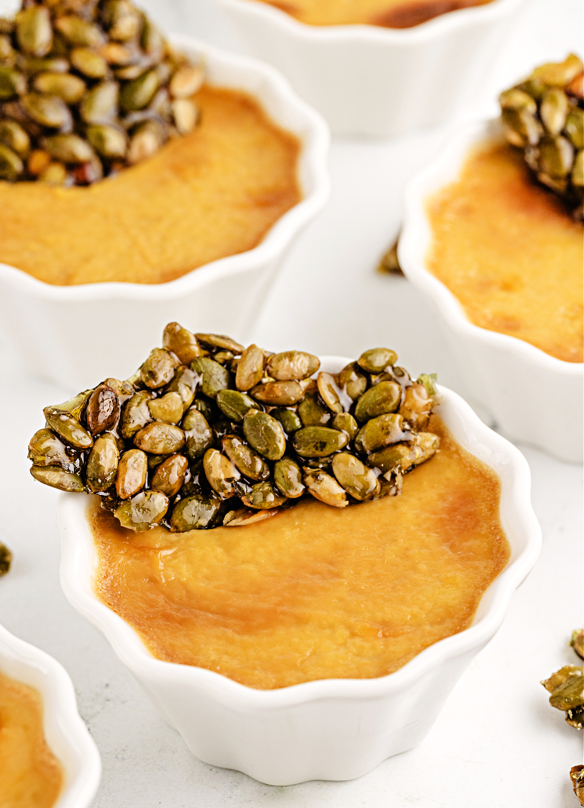 Pumpkin Chai Pots de Crème by Noble Pig topped with glossy pumpkin seed brittle, showing the silky baked custard texture up close.