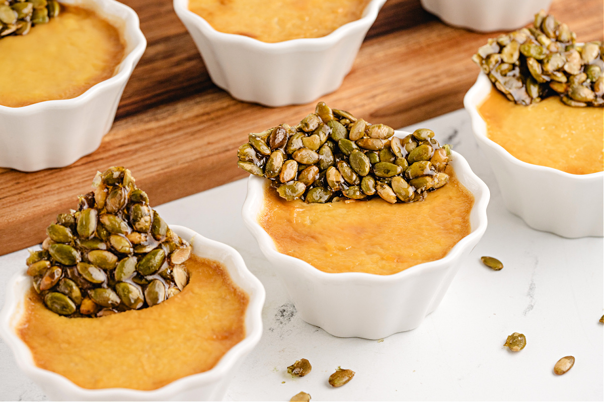 Pumpkin Chai Pots de Crème by Noble Pig arranged in white ramekins with crisp pepita brittle for a grown-up fall dessert.