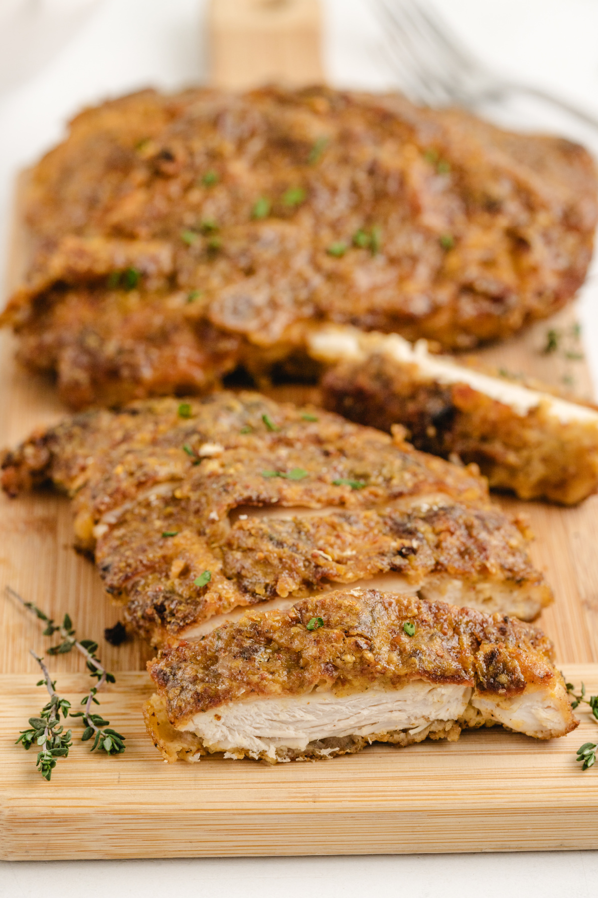 Crispy Glazed Chicken Cutlet Sliced on Board Sliced maple mustard glazed chicken cutlet on a wooden cutting board with fresh thyme
