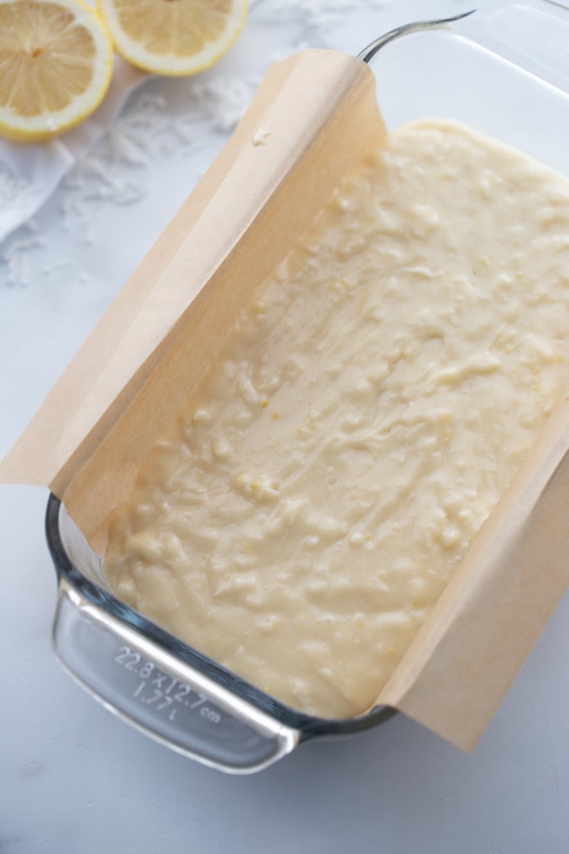 Lemon loaf batter in baking pan with parchment overhang Lemon loaf batter in a baking pan with parchment paper overhang, ready for baking.