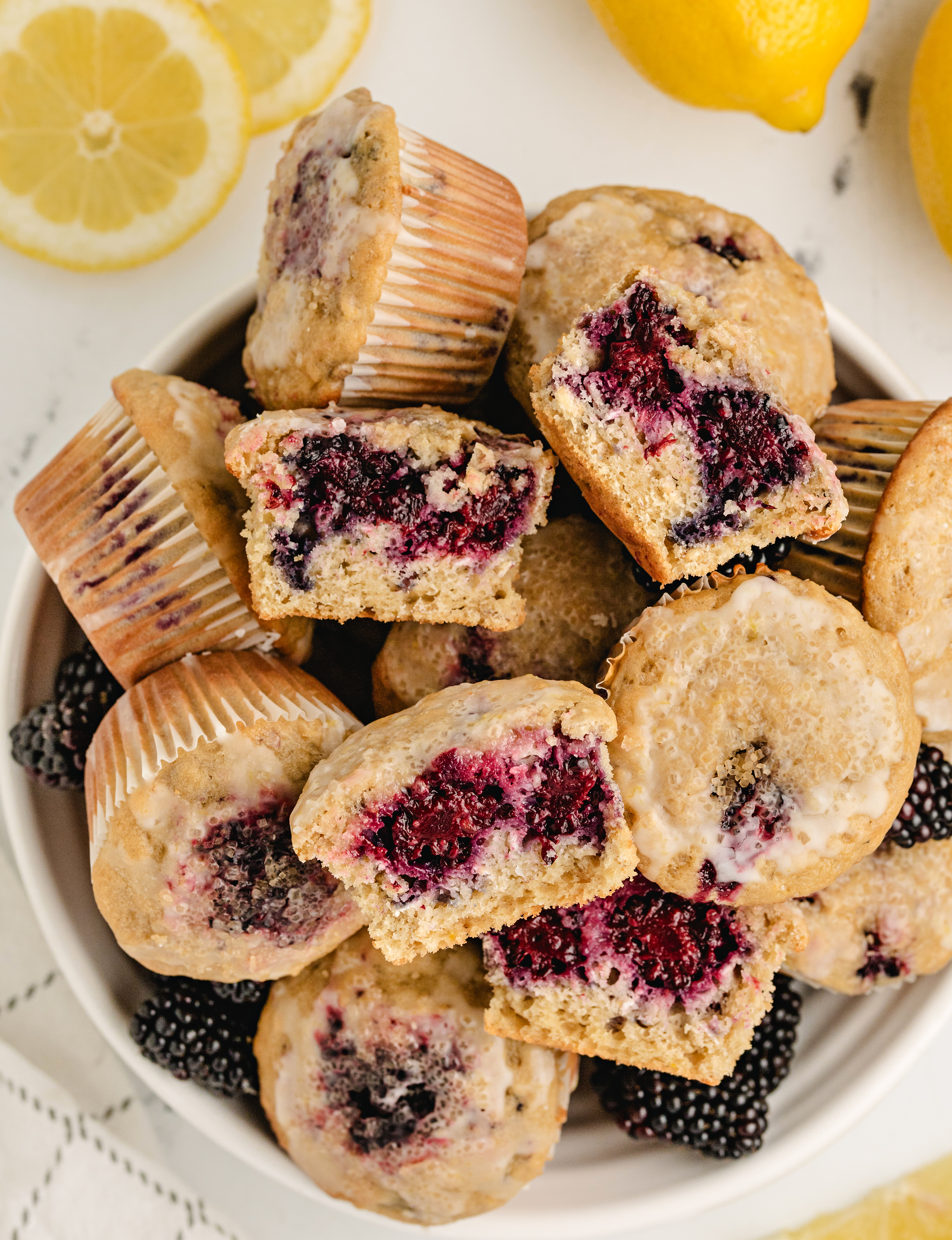 blackberry muffins with lemon glaze and oat batter halved lemon blackberry muffins with oats in a white bowl surrounded by fresh fruit