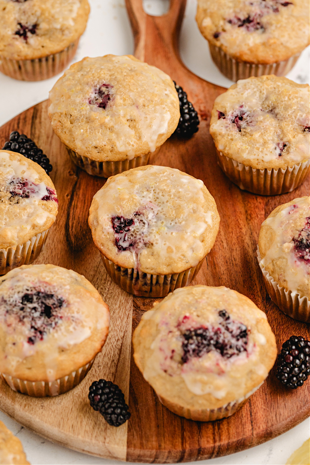 glazed blackberry oat muffins on serving board oat muffins with blackberries and lemon glaze arranged on a wooden board