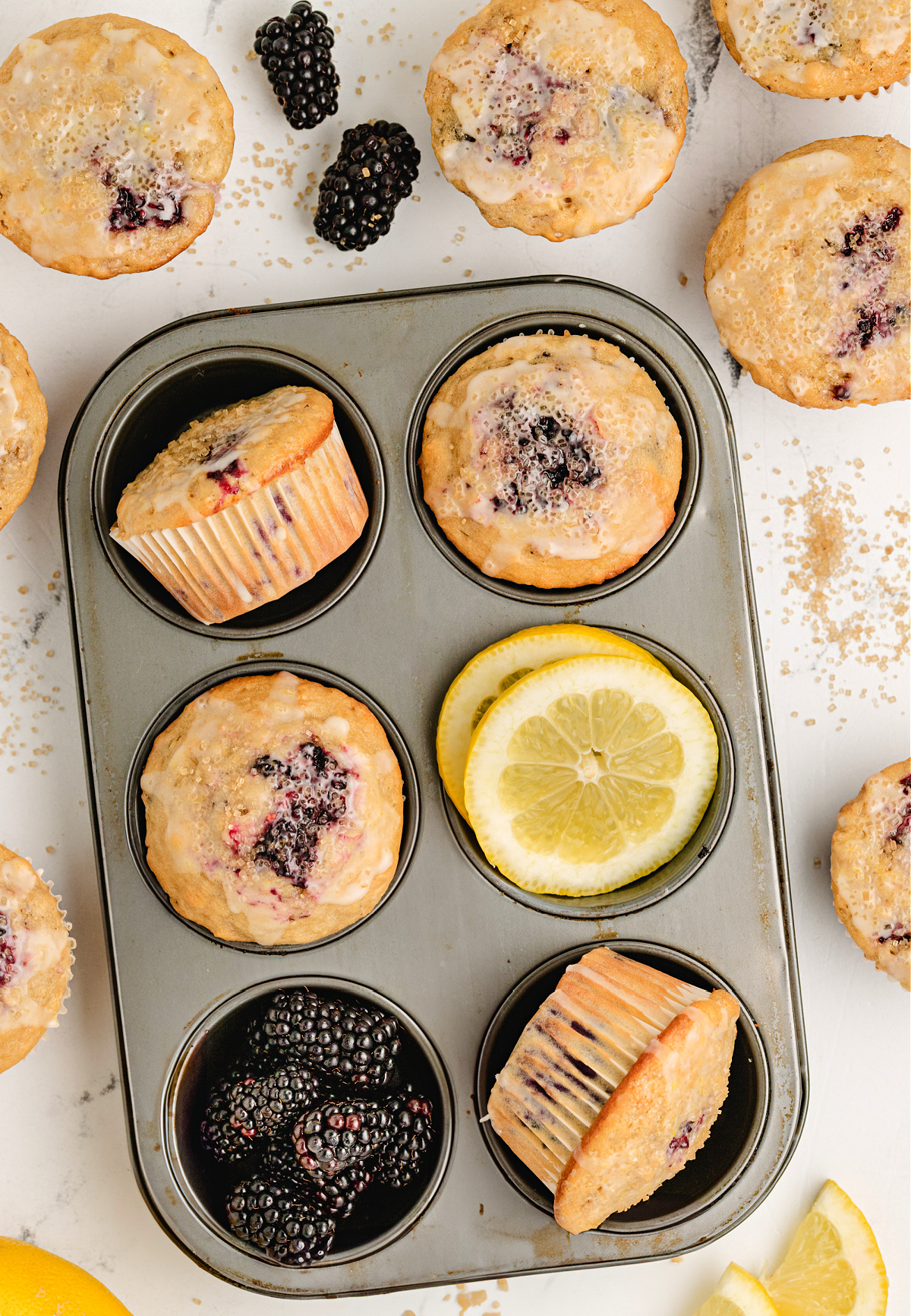 blackberry lemon muffins with coarse sugar baked in muffin tin muffin tin filled with baked lemon blackberry muffins, fresh berries, and lemon slices for garnish