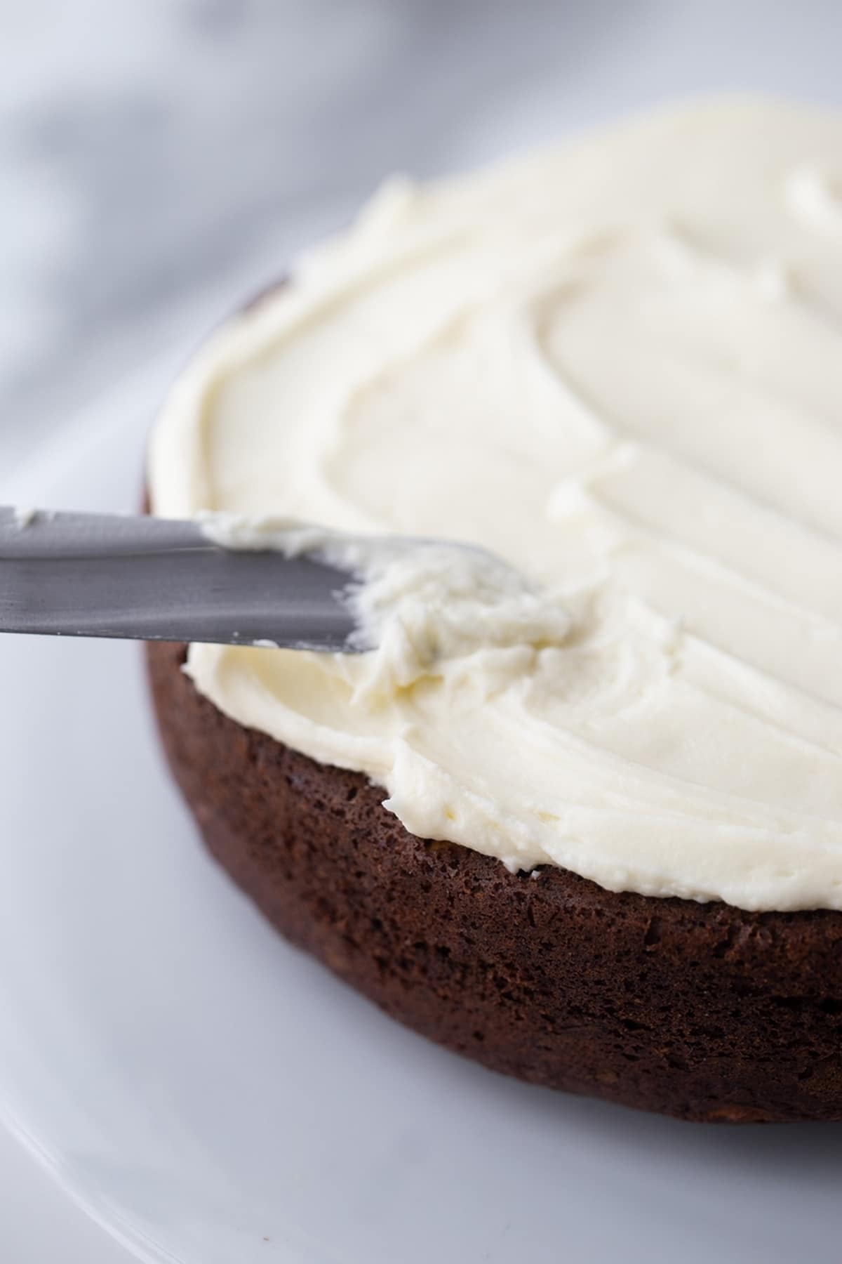 Spreading cream cheese frosting on top of a homemade chocolate zucchini cake layer.
