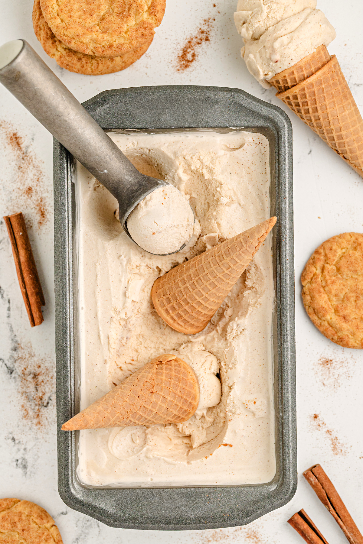 Snickerdoodle ice cream in loaf pan with cones and cinnamon sticks. Loaf pan filled with homemade snickerdoodle ice cream and sugar cones.