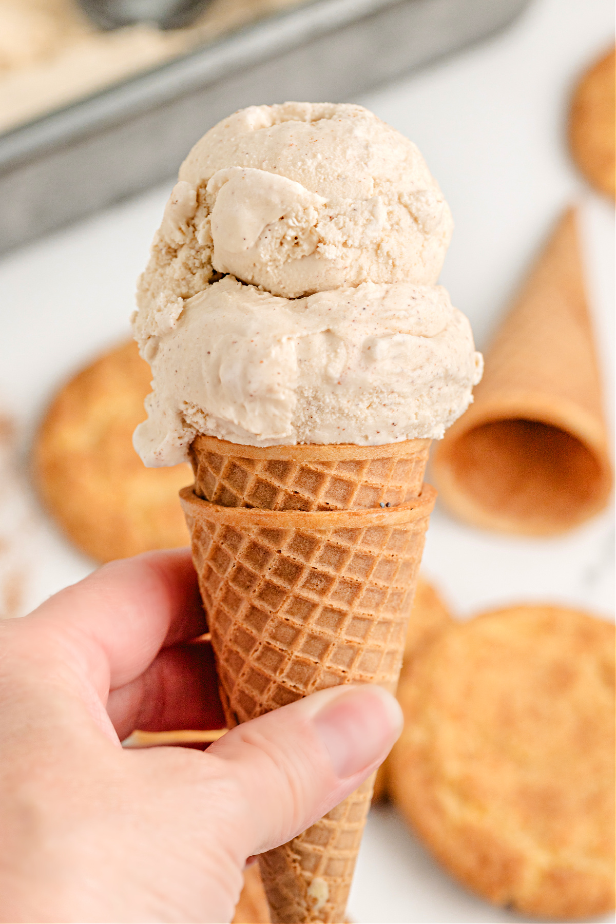 Waffle cone with scoops of cinnamon ice cream. Hand holding a waffle cone with two scoops of cinnamon-spiced ice cream.