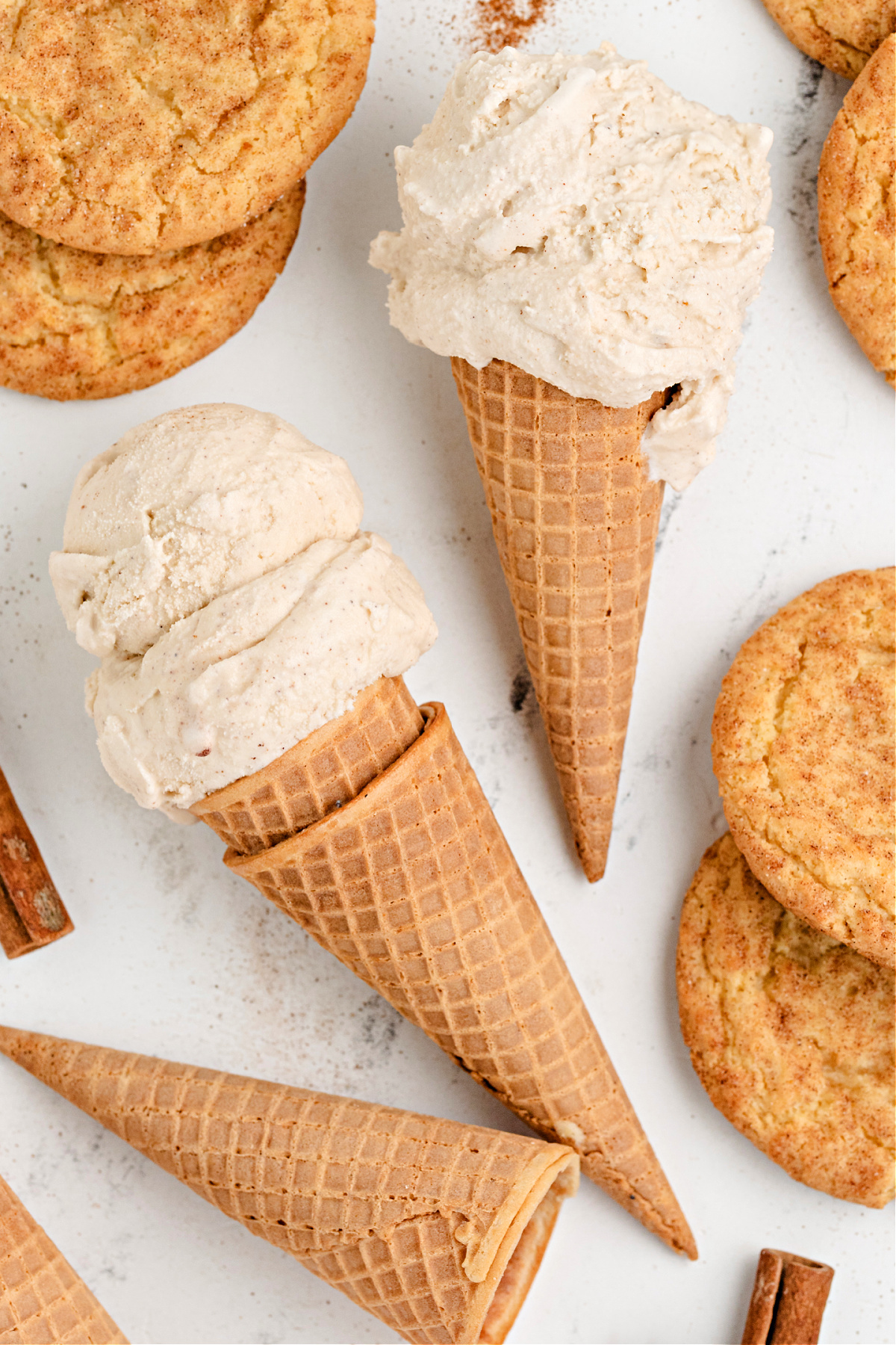 Cinnamon-sugar ice cream cones with snickerdoodle cookies. Two ice cream cones surrounded by snickerdoodle cookies.