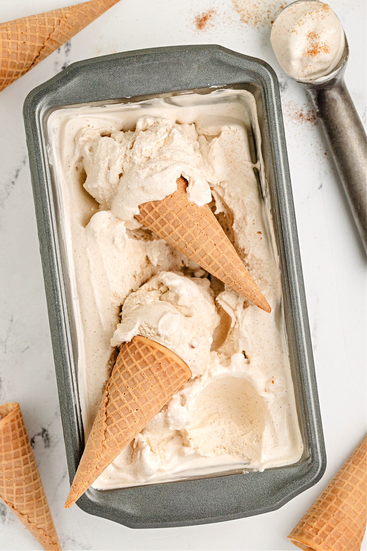 Snickerdoodle ice cream loaf pan with cones. Loaf pan of churned snickerdoodle ice cream with two cones resting on top.