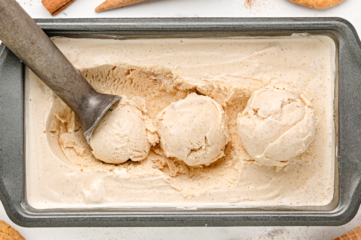 Loaf pan of cinnamon-sugar ice cream with scoops. Three scoops of cinnamon ice cream in a loaf pan with a metal scoop.