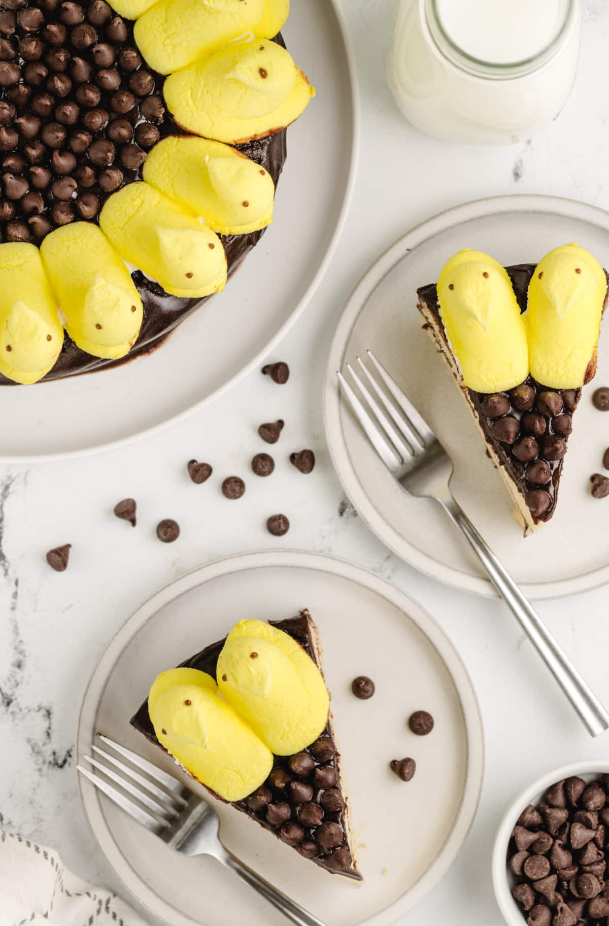 Top-down view of two slices of yellow cake with chocolate frosting, Peeps, and chocolate chips on the plate.
