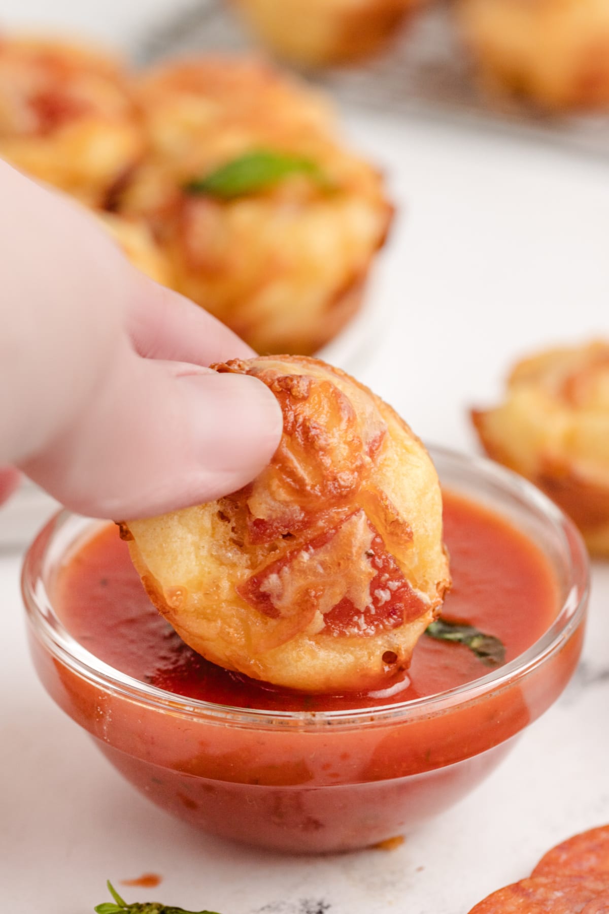 A single pizza puff being dipped into a small bowl of warm pizza sauce, with cheese and pepperoni visible in the bite.