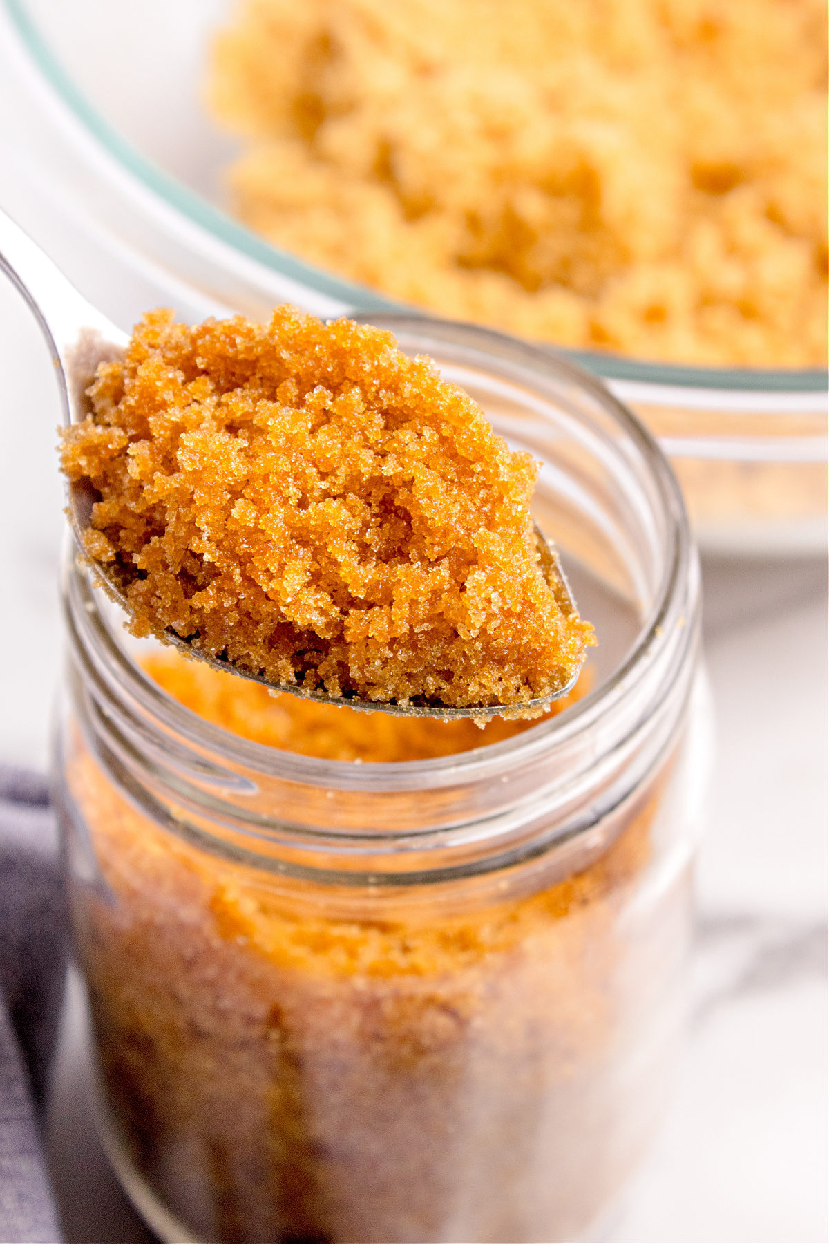 A spoonful of homemade brown sugar being lifted from a glass jar, showing the soft, moist texture and rich molasses color.