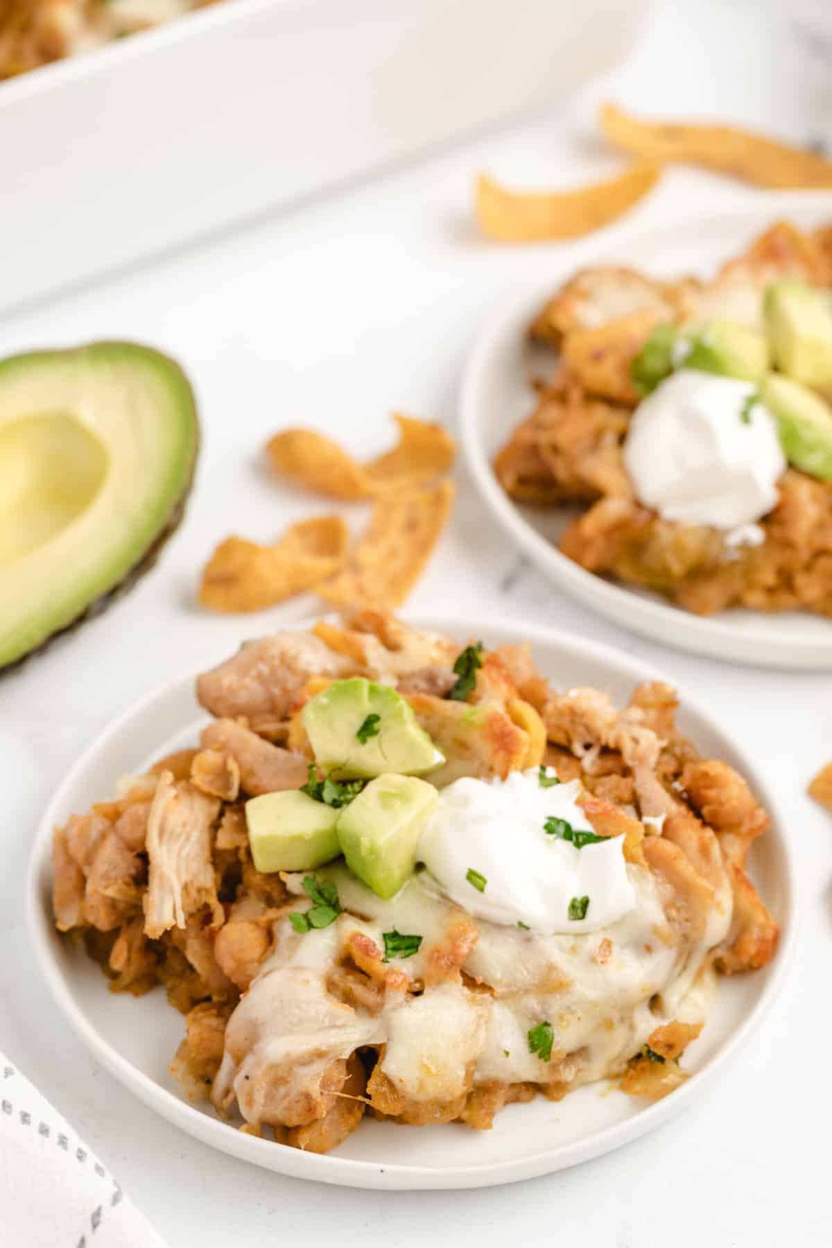 Two plates of Chicken Frito Pie Casserole served with sour cream, avocado slices, and chopped cilantro.