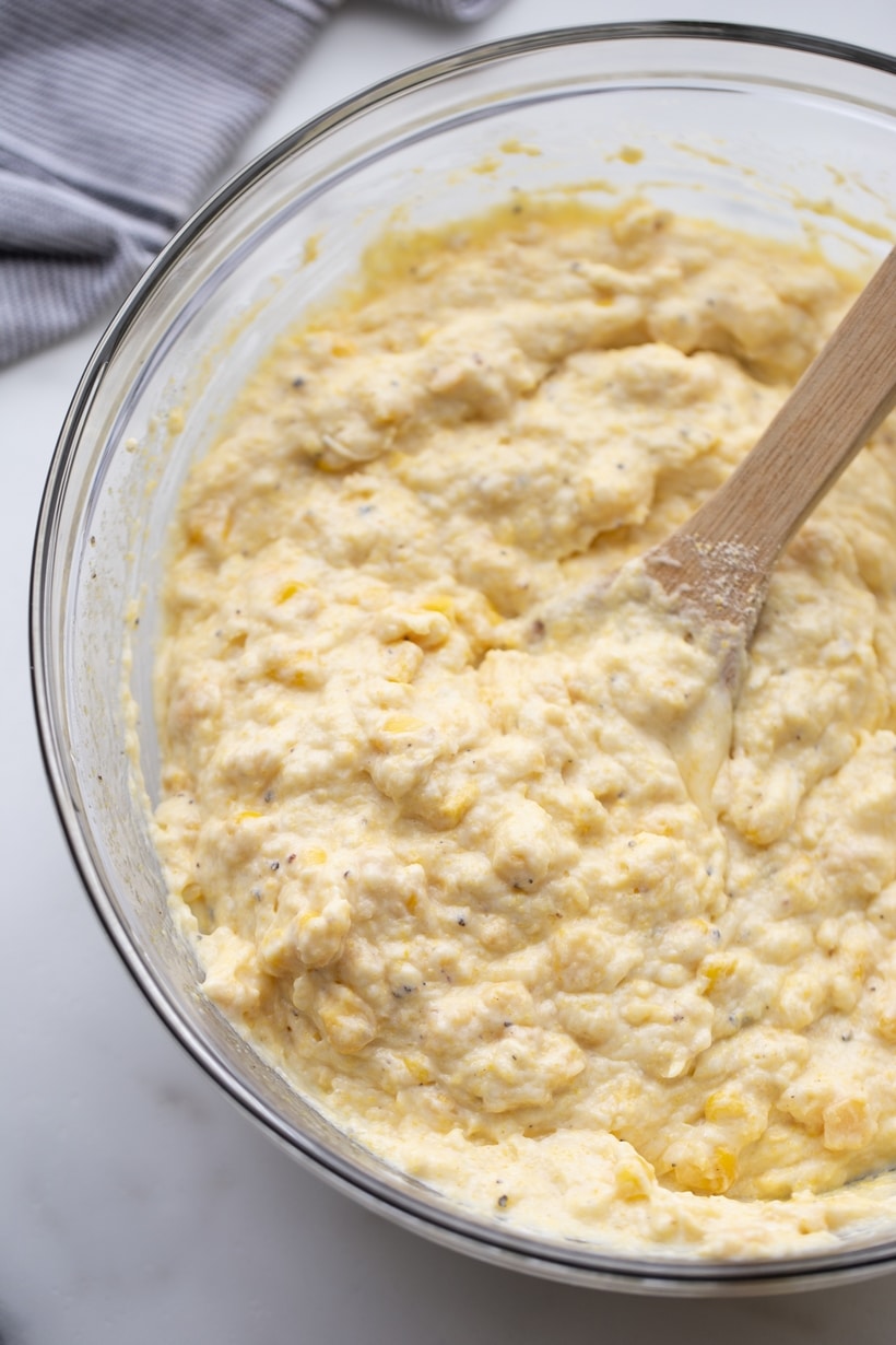 Corn Pudding batter Corn pudding batter fully combined in a mixing bowl, with a wooden spoon resting inside.