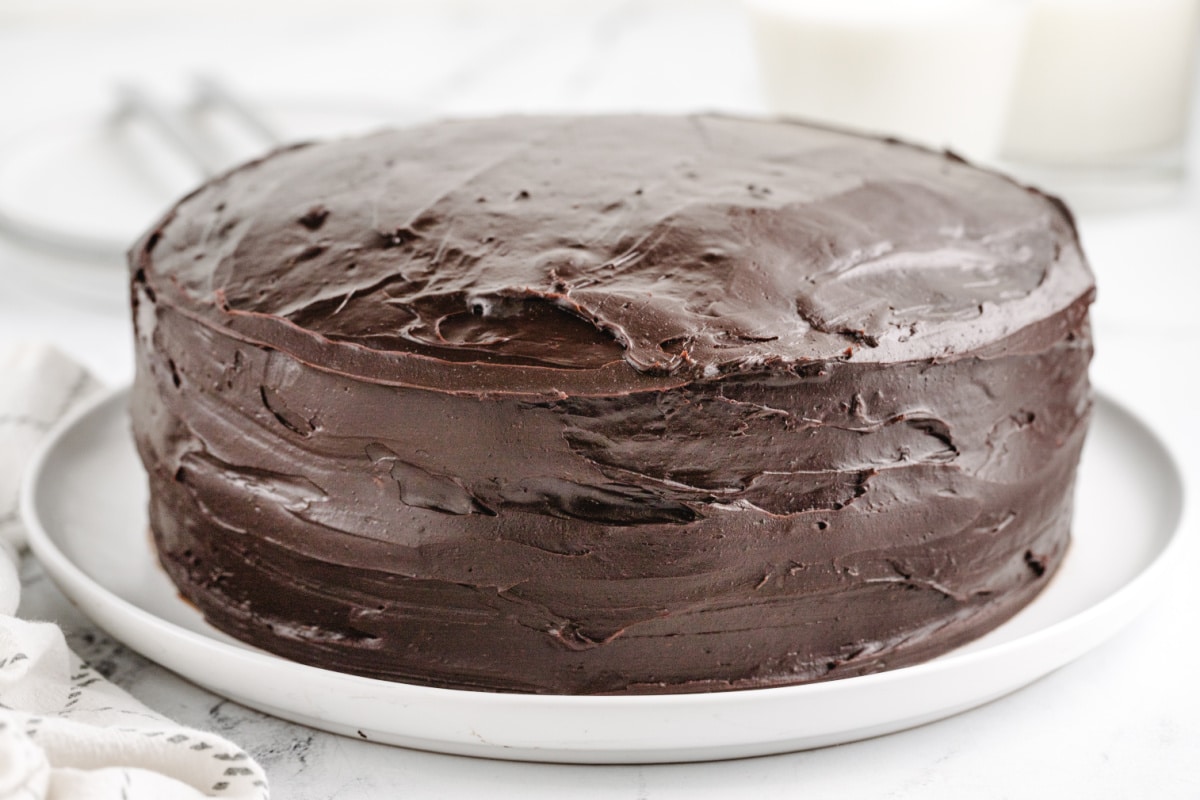 A whole Old-Fashioned Chocolate Cake with Glossy Chocolate Icing Whole old-fashioned chocolate cake on a cake stand, with thick chocolate icing covering the top and sides.