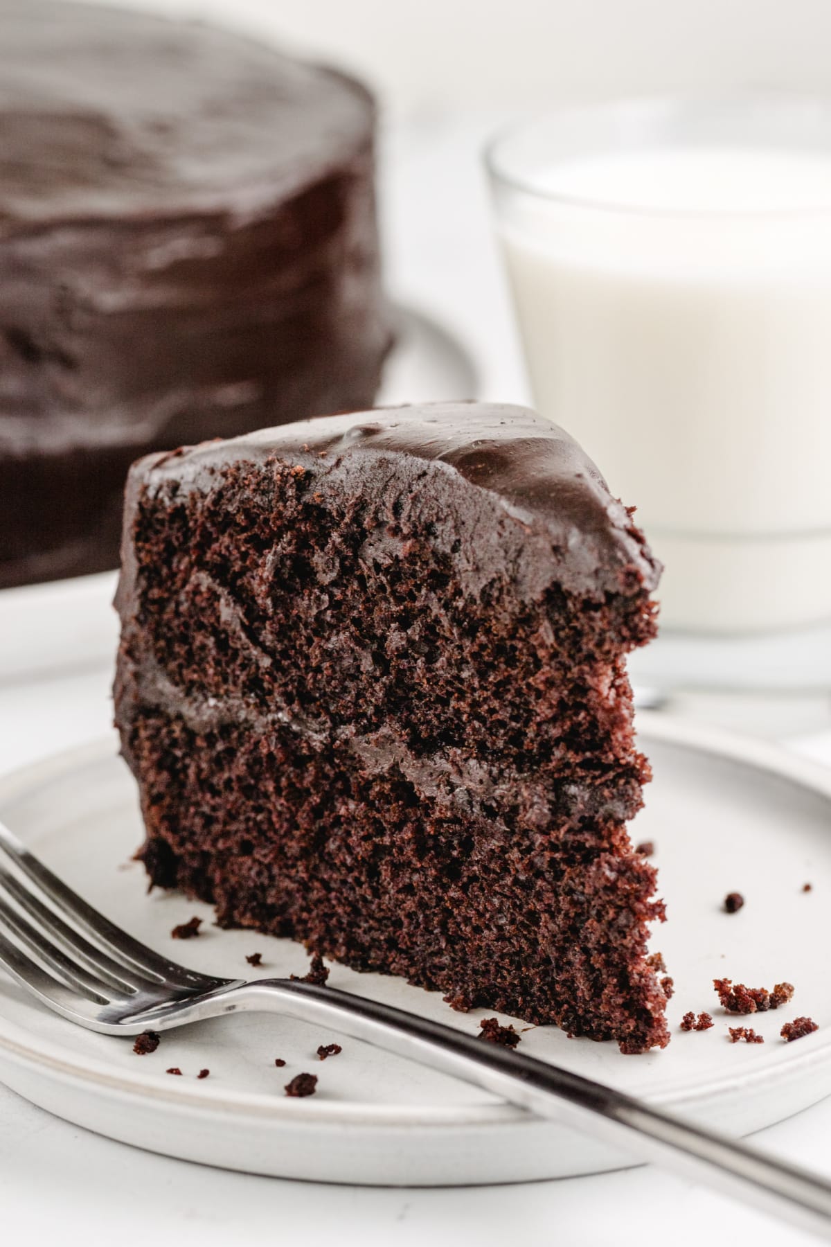 Old-Fashioned Chocolate Cake with Glossy Chocolate Icing with a fork a slice of chocolate cake on a plate with a bite taken out, showing the rich chocolate color.