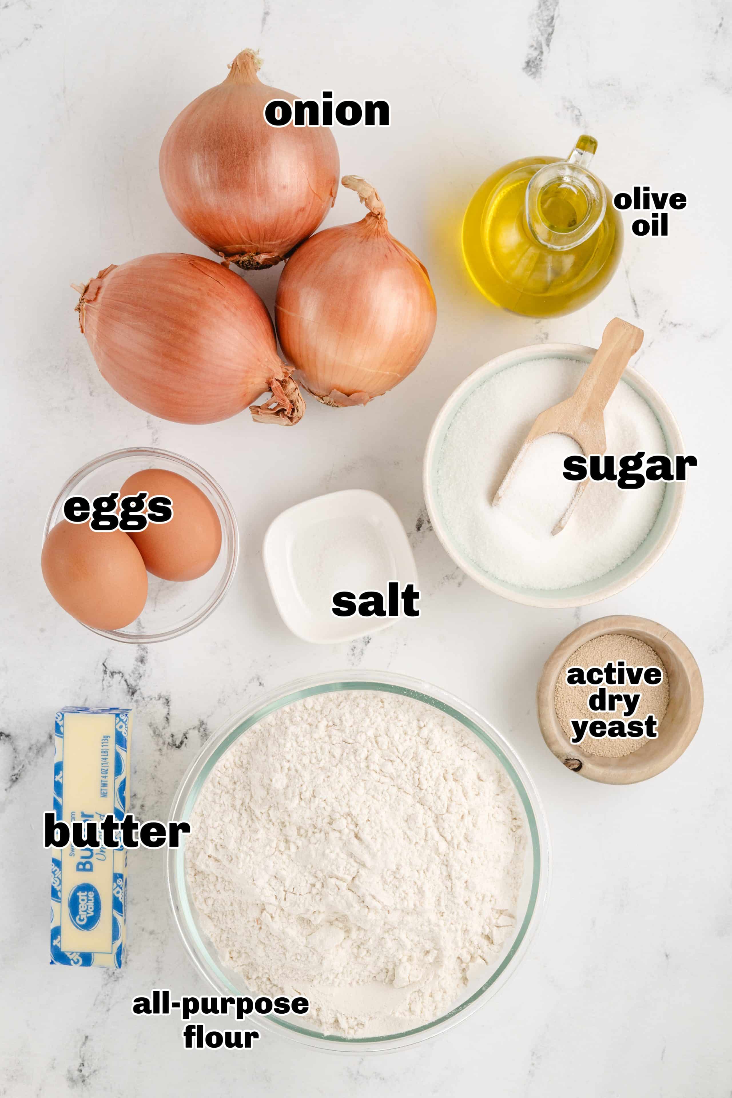 A display of ingredients for no-knead onion rolls, including flour, eggs, yeast, butter, and caramelized onions.