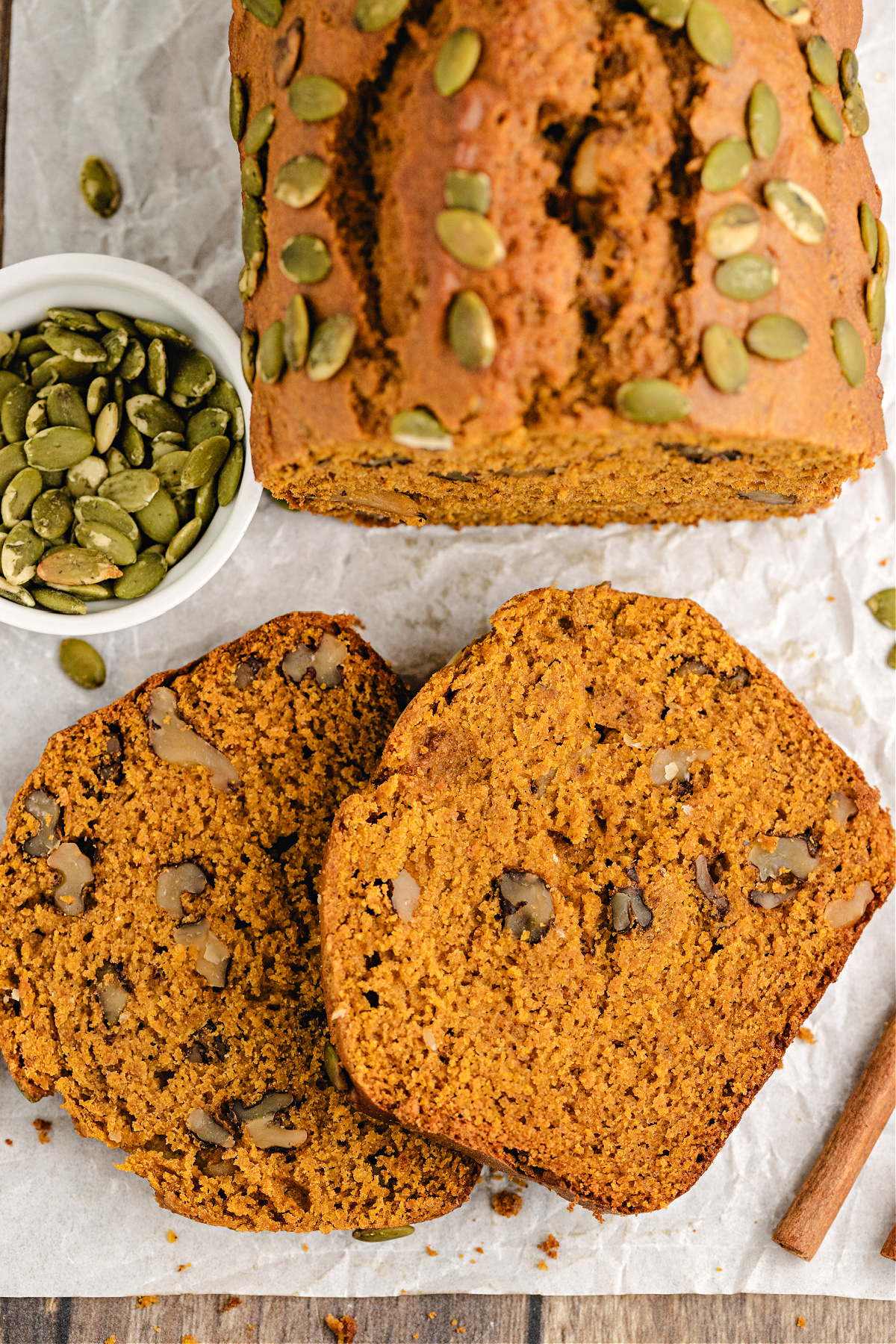 Pumpkin walnut bread slices on parchment with pepitas.