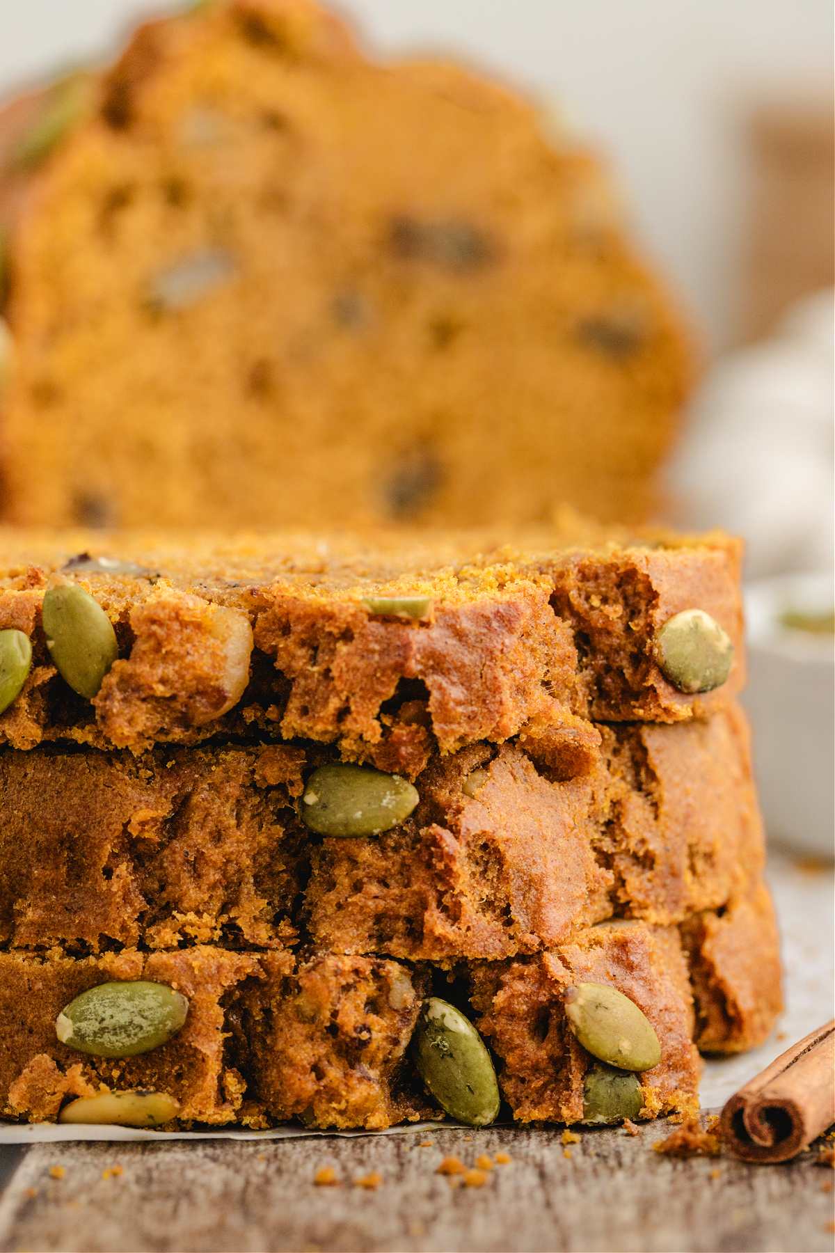 Soft pumpkin loaf slices stacked with pepitas on the crust.