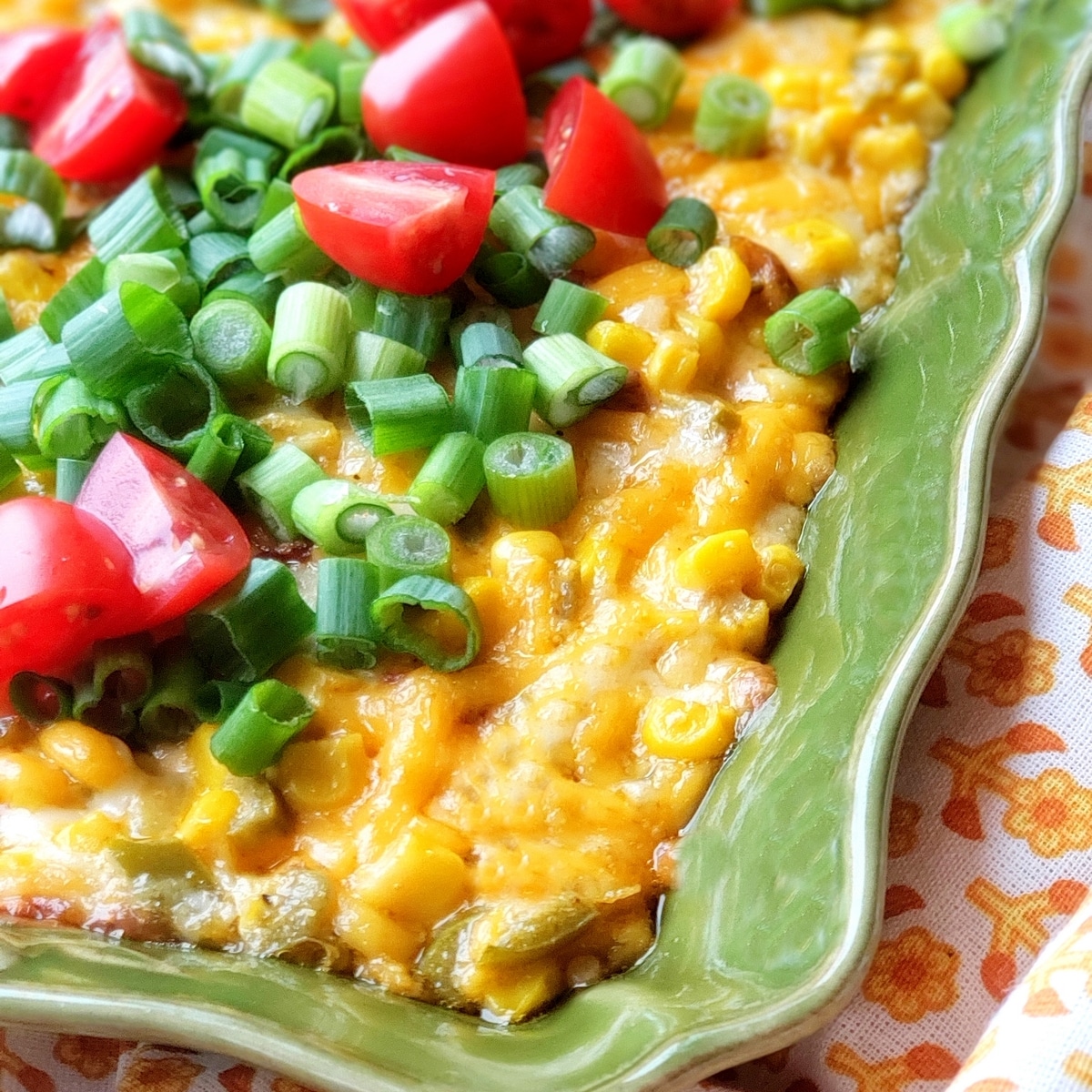 Overhead view of hot cheesy corn dip garnished with green onions and diced tomatoes.