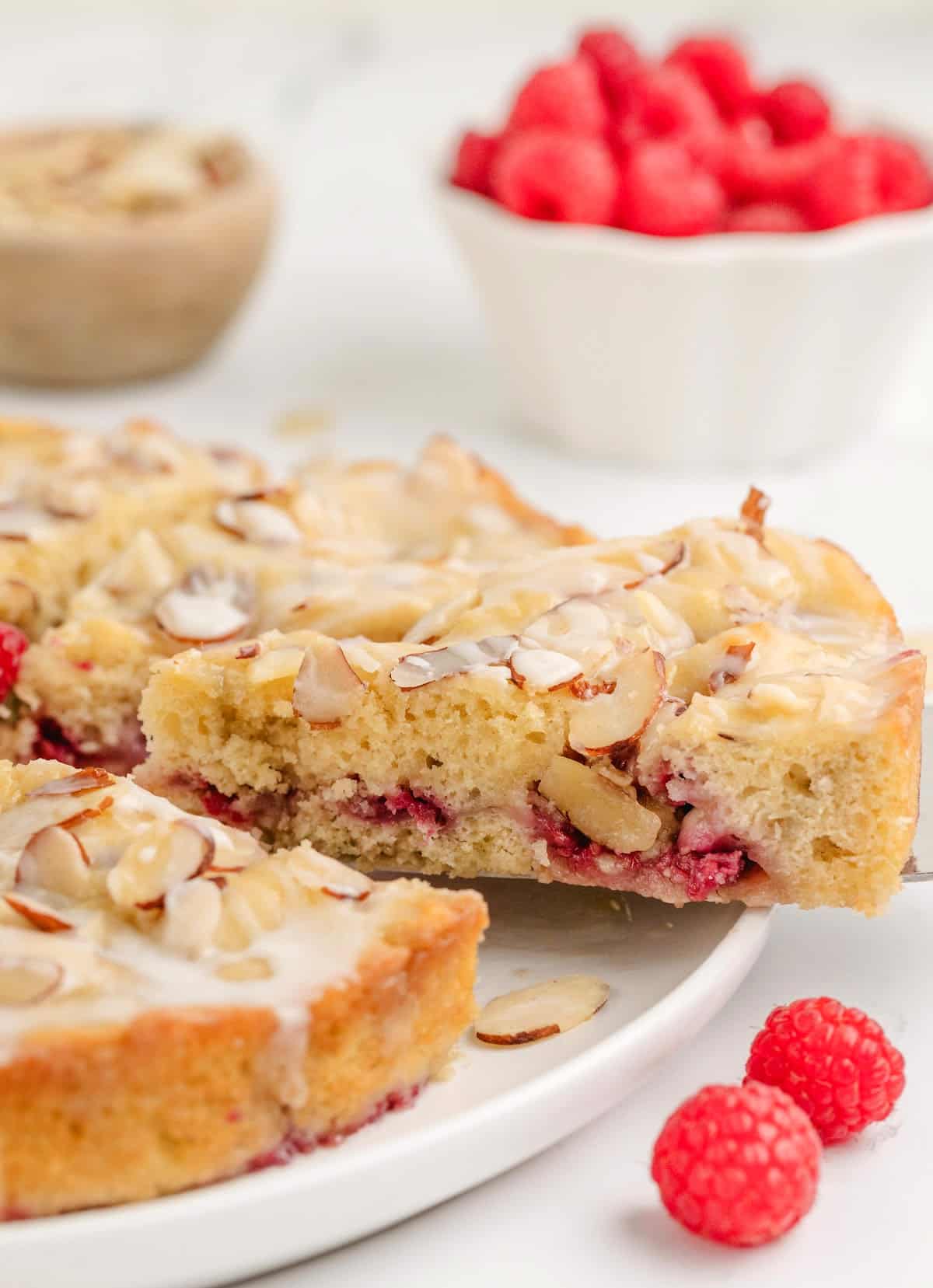 slicing Raspberry Almond Coffee Cake A single slice being lifted from the coffee cake, showing the soft texture, juicy raspberry filling, and crisp almond topping.