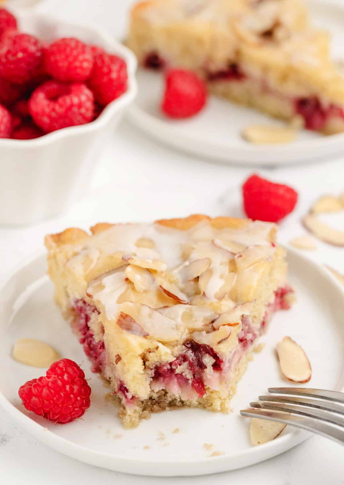 one slice of Raspberry Almond Coffee Cake Close-up of a raspberry almond coffee cake slice with a bite removed, showing the soft crumb, juicy raspberries, and crunchy almond topping.