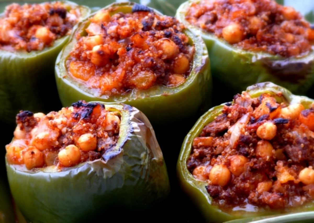 Mediterranean-Style Stuffed Peppers in a baking dish Side view of a stuffed pepper cut in half, revealing the quinoa, beef, chickpeas, and apricots inside the roasted bell pepper.