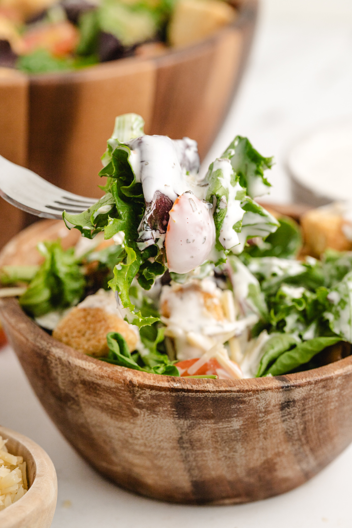 Copycat Spaghetti Factory Creamy Pesto Dressing on Salad Fork lifting greens and tomatoes from a wooden bowl with creamy pesto dressing