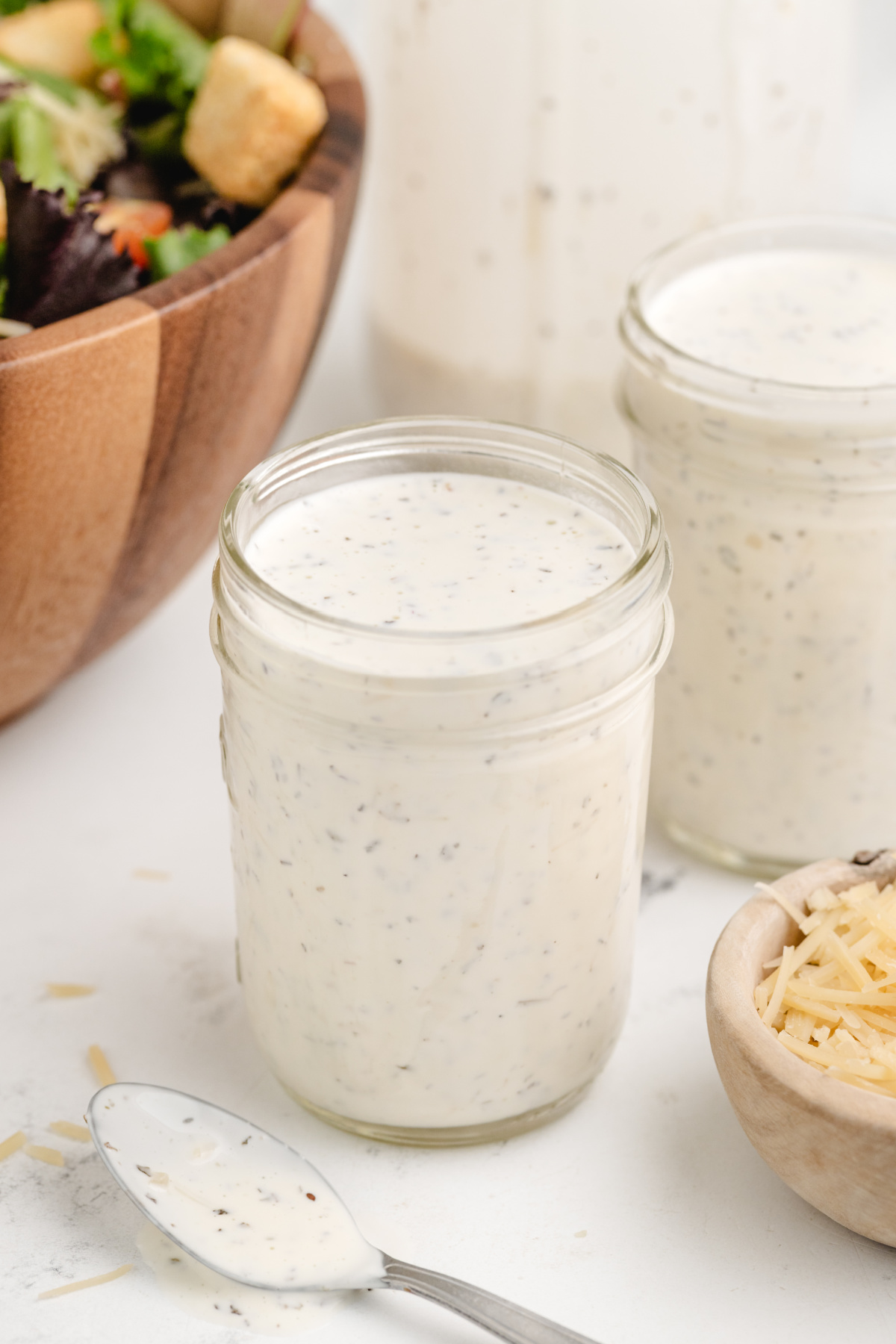 Spaghetti Factory Copycat Pesto Dressing in a Jar Mason jar filled with homemade creamy pesto dressing next to grated Parmesan and salad