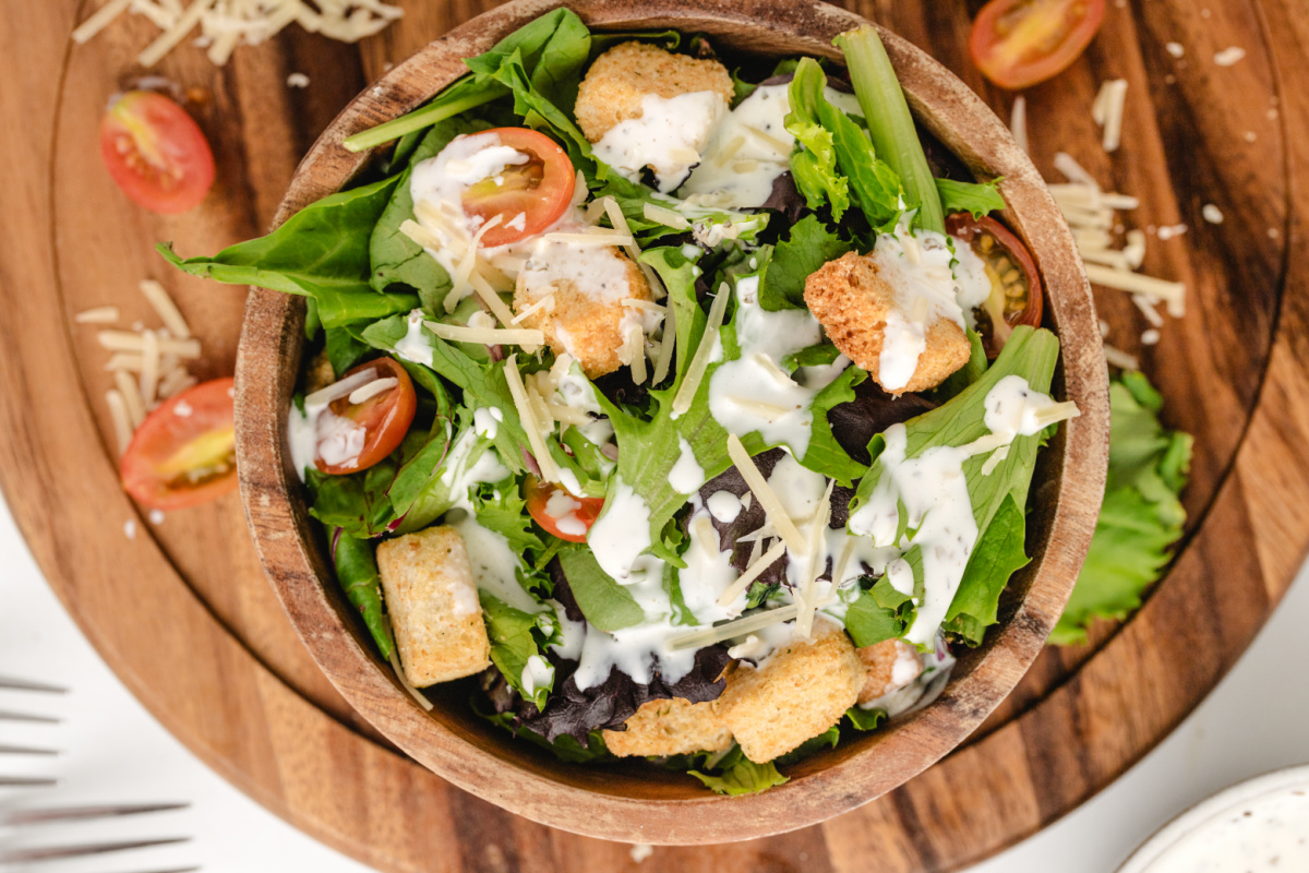 Copycat Old Spaghetti Factory Salad with Creamy Pesto Dressing Overhead shot of salad drizzled with creamy pesto dressing and topped with croutons and cherry tomatoes