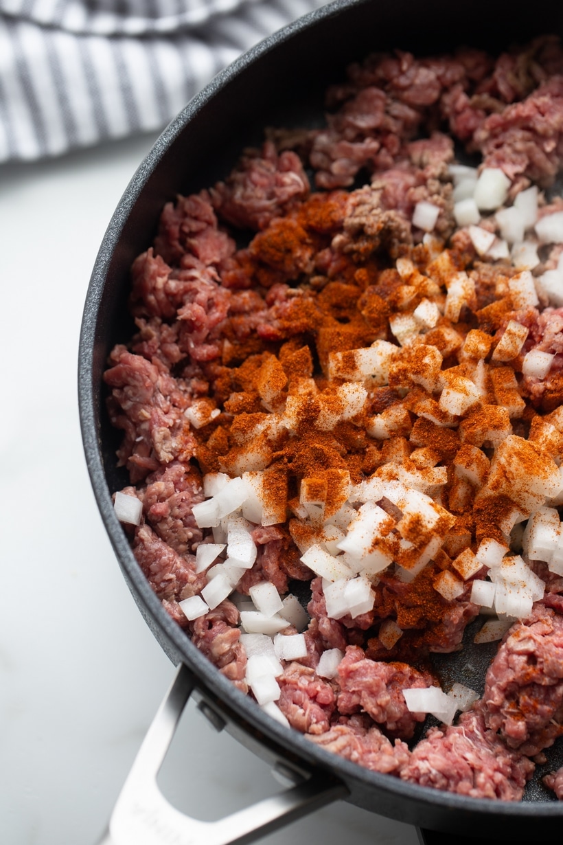 Raw ground beef, chopped onion, and chipotle powder in skillet before cooking
