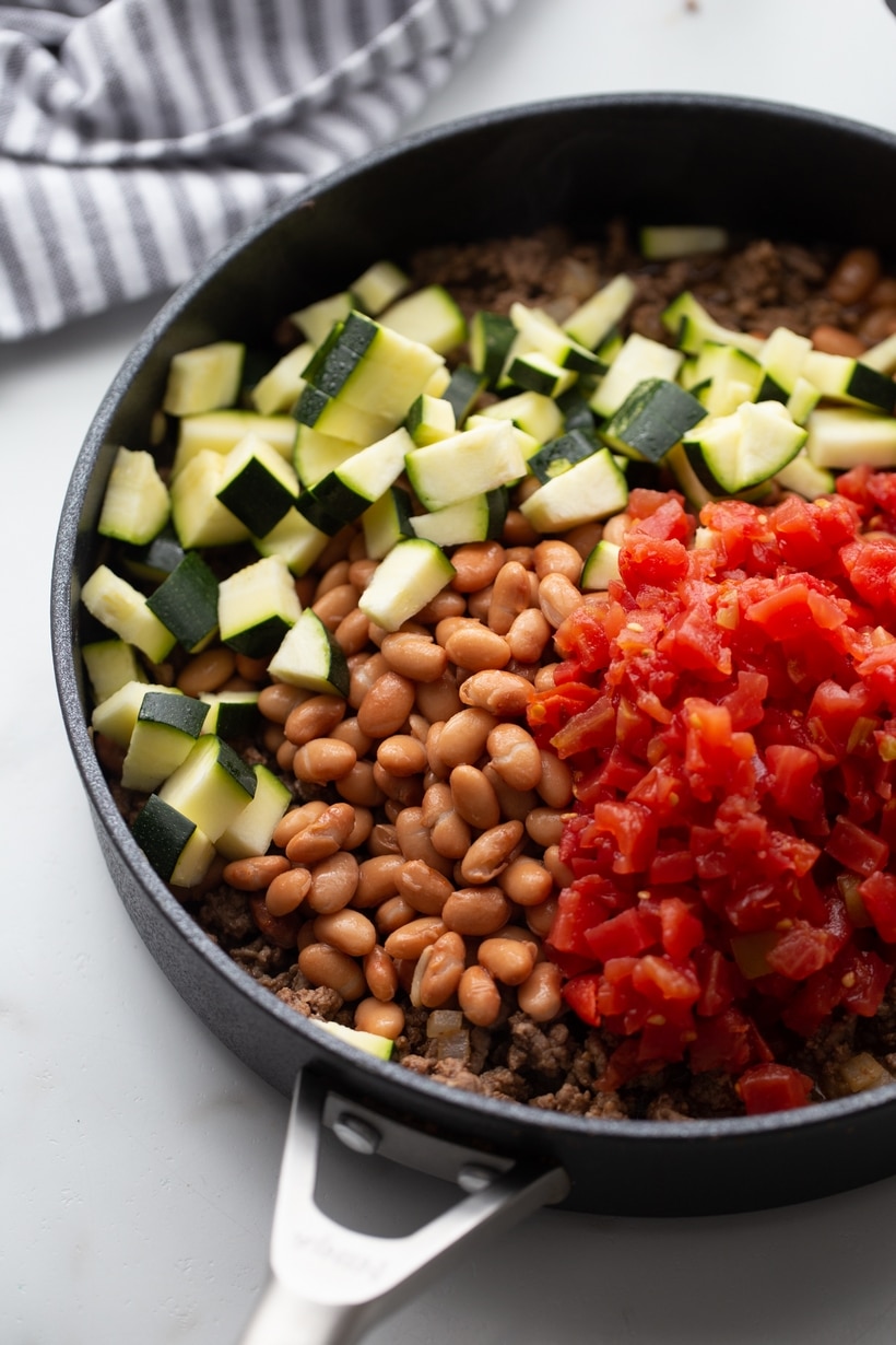 Zucchini, fire-roasted tomatoes, and pinto beans on top of browned beef in skillet