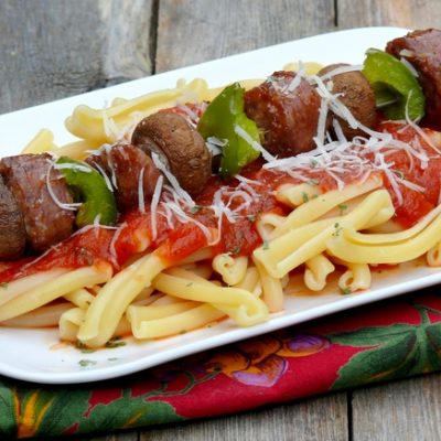 Sausage kabob sitting on top of pasta.