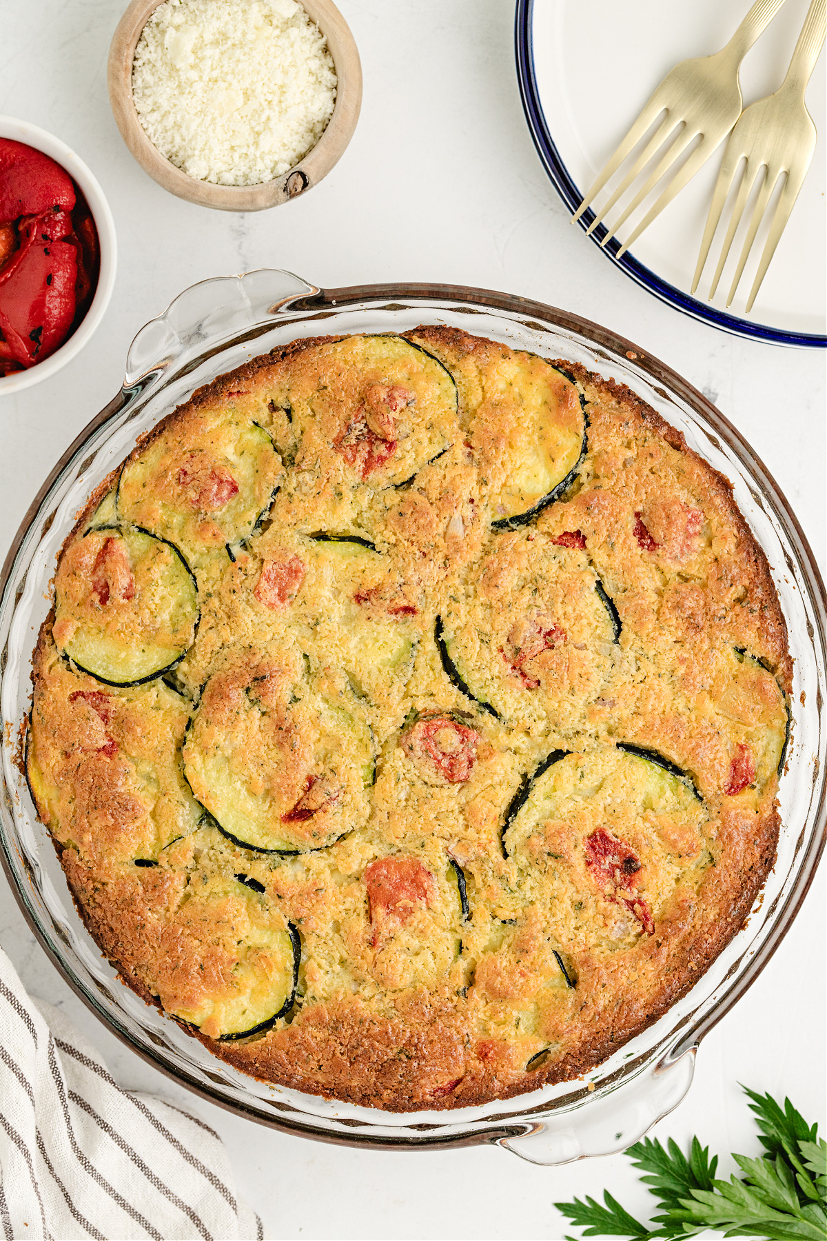 Bisquick vegetable pie with zucchini and pecorino romano Overhead shot of baked zucchini cheese pie ready to slice, with bowls of roasted pepper and grated cheese