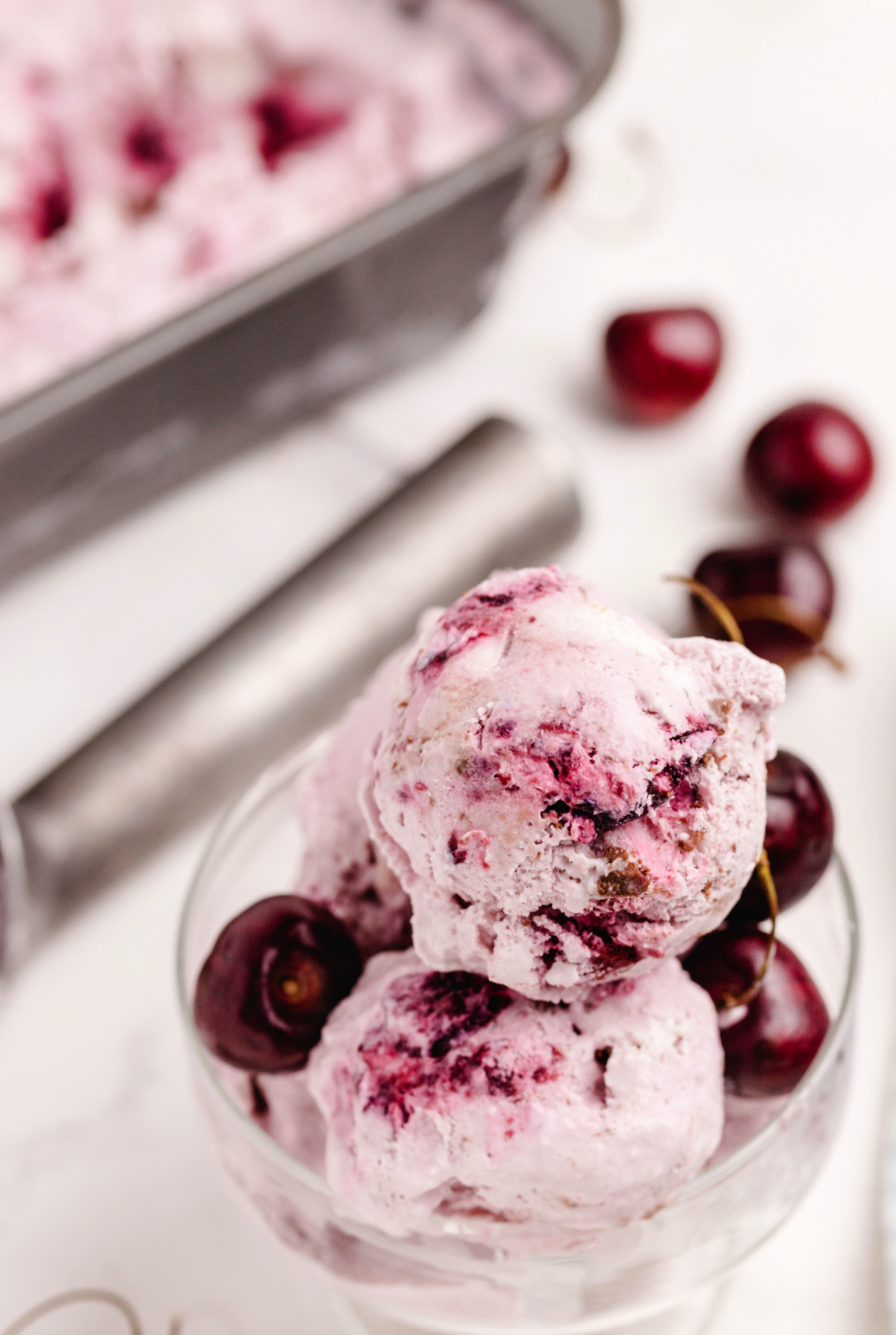 Scoops of fresh cherry coconut chocolate chip ice cream in a glass with whole cherries, highlighting creamy texture and real fruit.