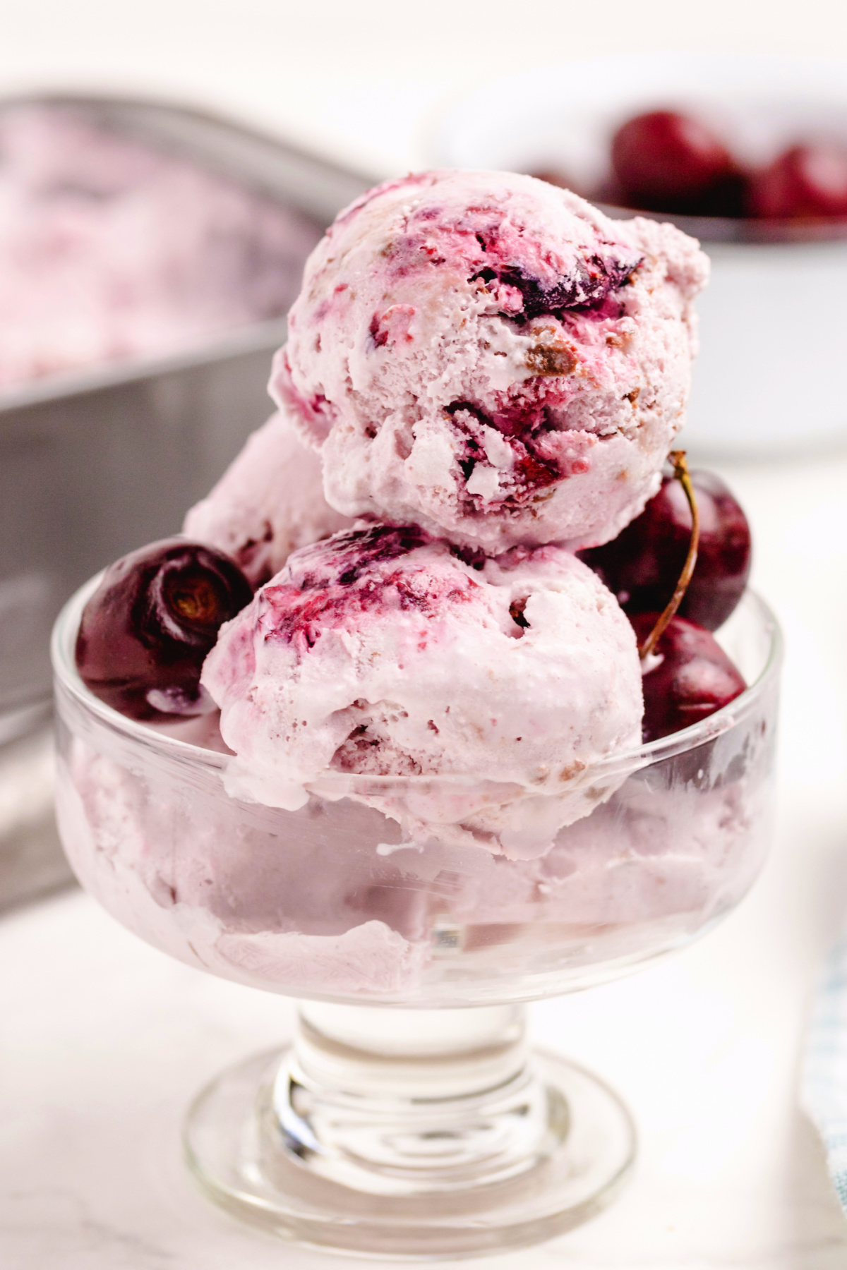 Glass dish with scoops of homemade cherry coconut chocolate chip ice cream, showing swirls of cherry and chunks of chocolate.