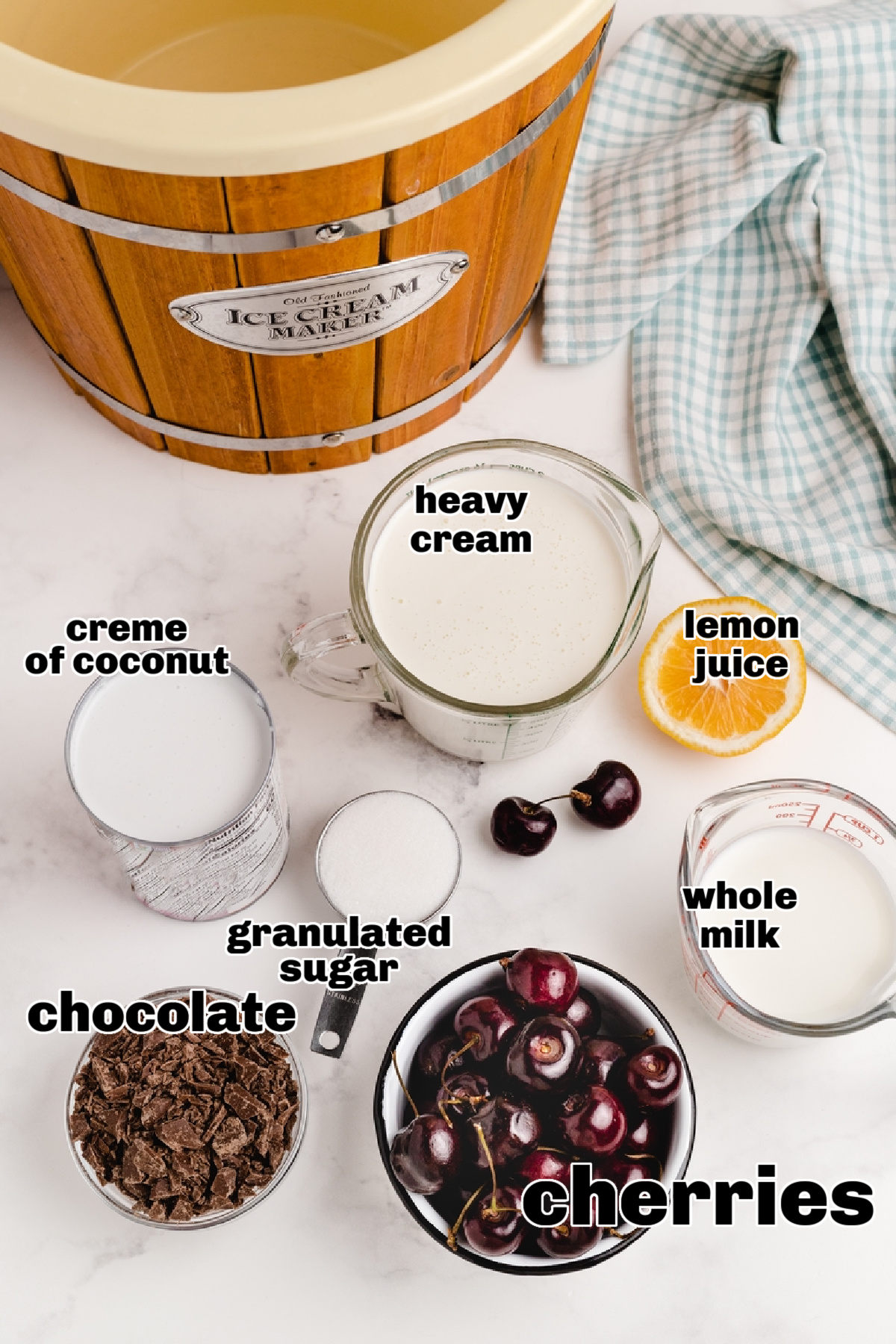 Overhead view of labeled ingredients for cherry coconut chocolate chip ice cream, including cherries, crème of coconut, and chopped chocolate.
