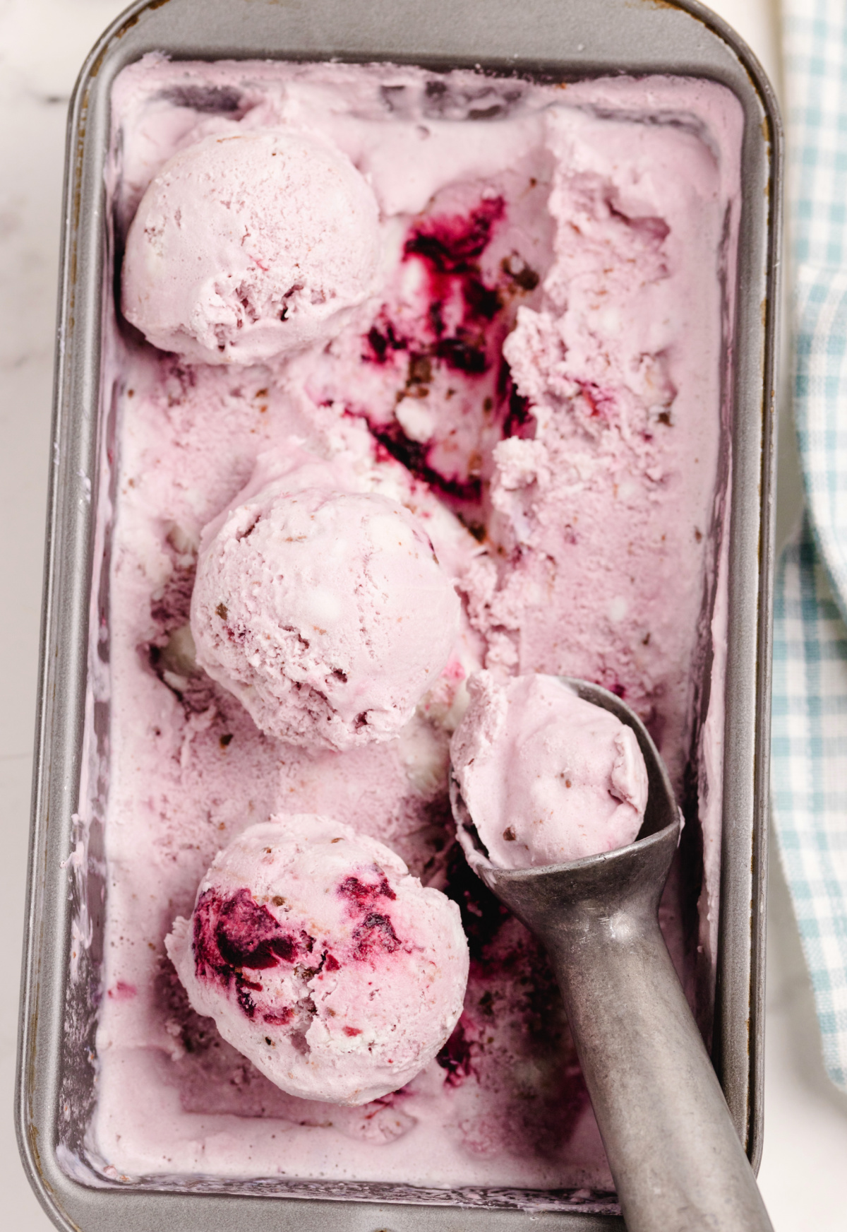 Container of churned fresh cherry coconut chocolate chip ice cream with a scoop and visible cherry swirls and chocolate chunks.
