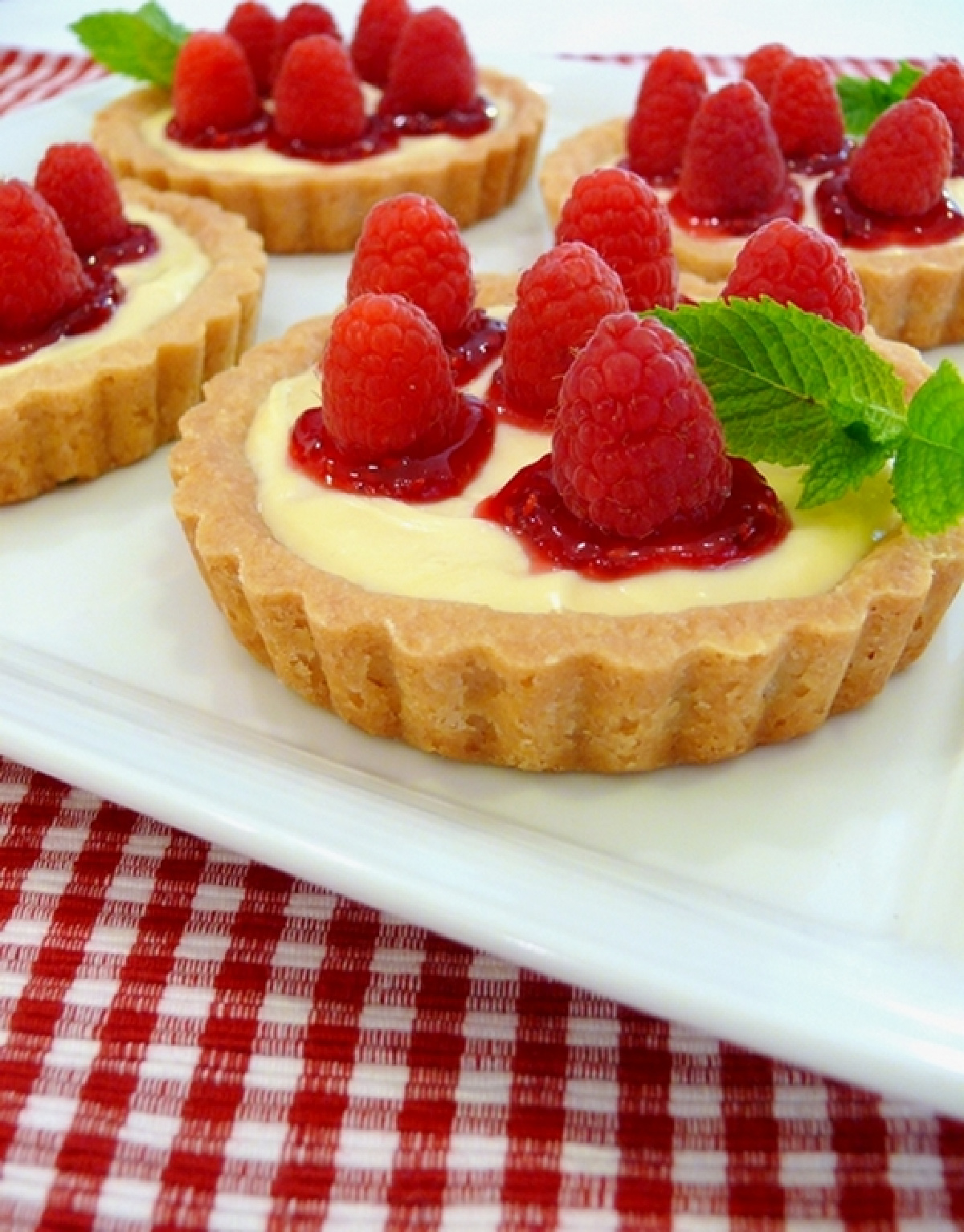 Raspberry Lemon Tartlets topped with fresh raspberries and raspberry jam in buttery shortbread tart shells.