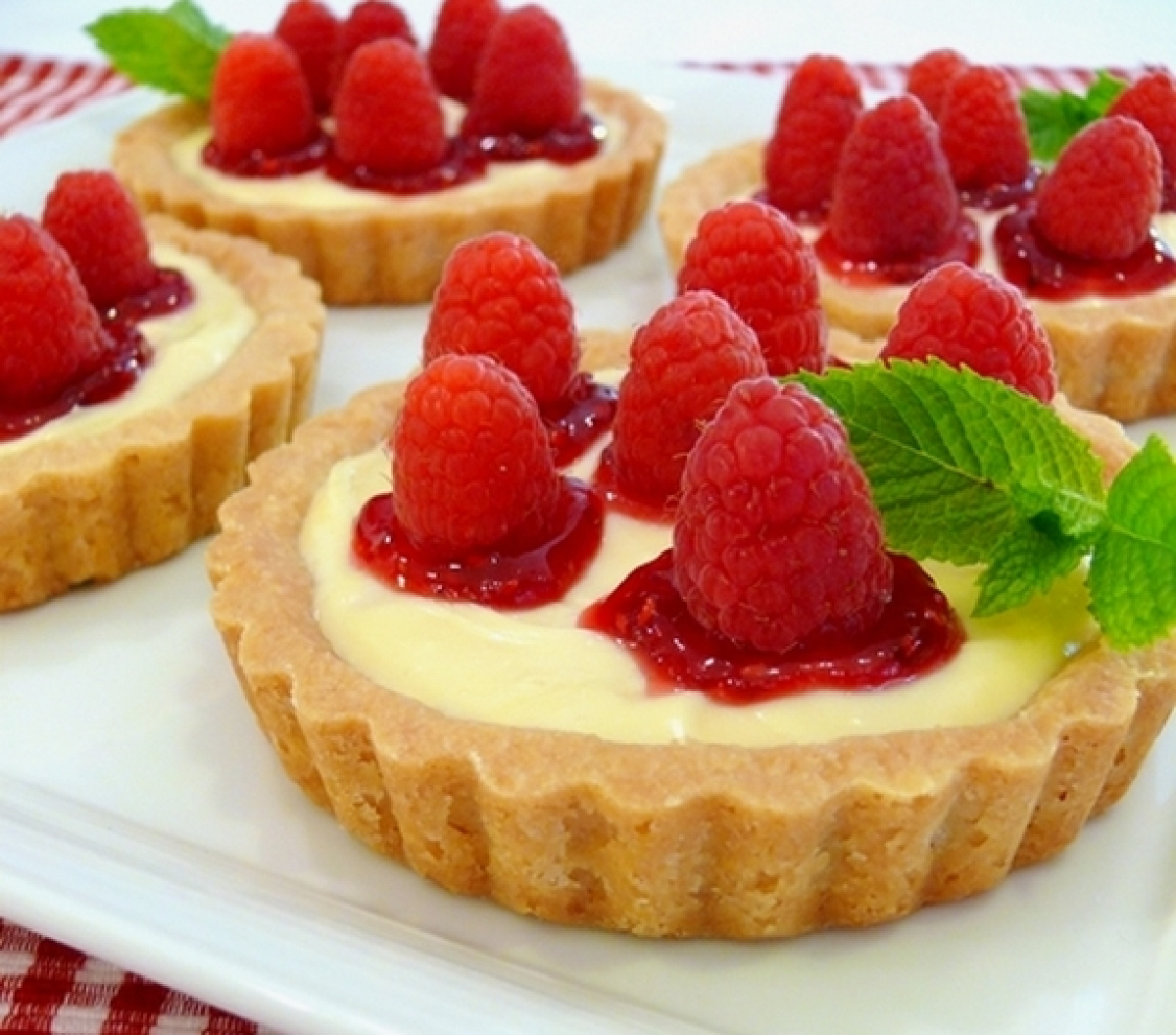 Close-up of raspberry lemon tartlets with lemon curd filling, raspberry jam, fresh raspberries, and a buttery shortbread crust.