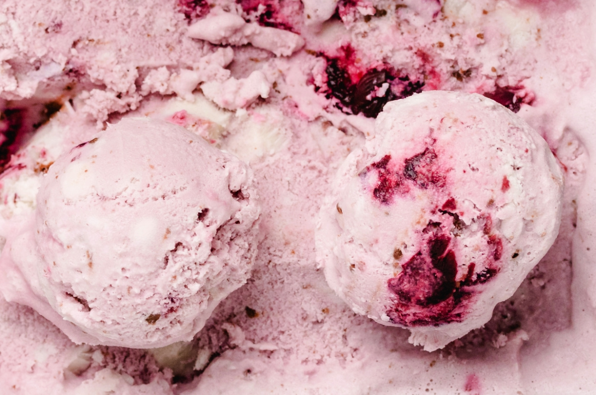 Close-up of two scoops of cherry coconut chocolate chip ice cream showing the real fruit pieces and rich creamy texture.