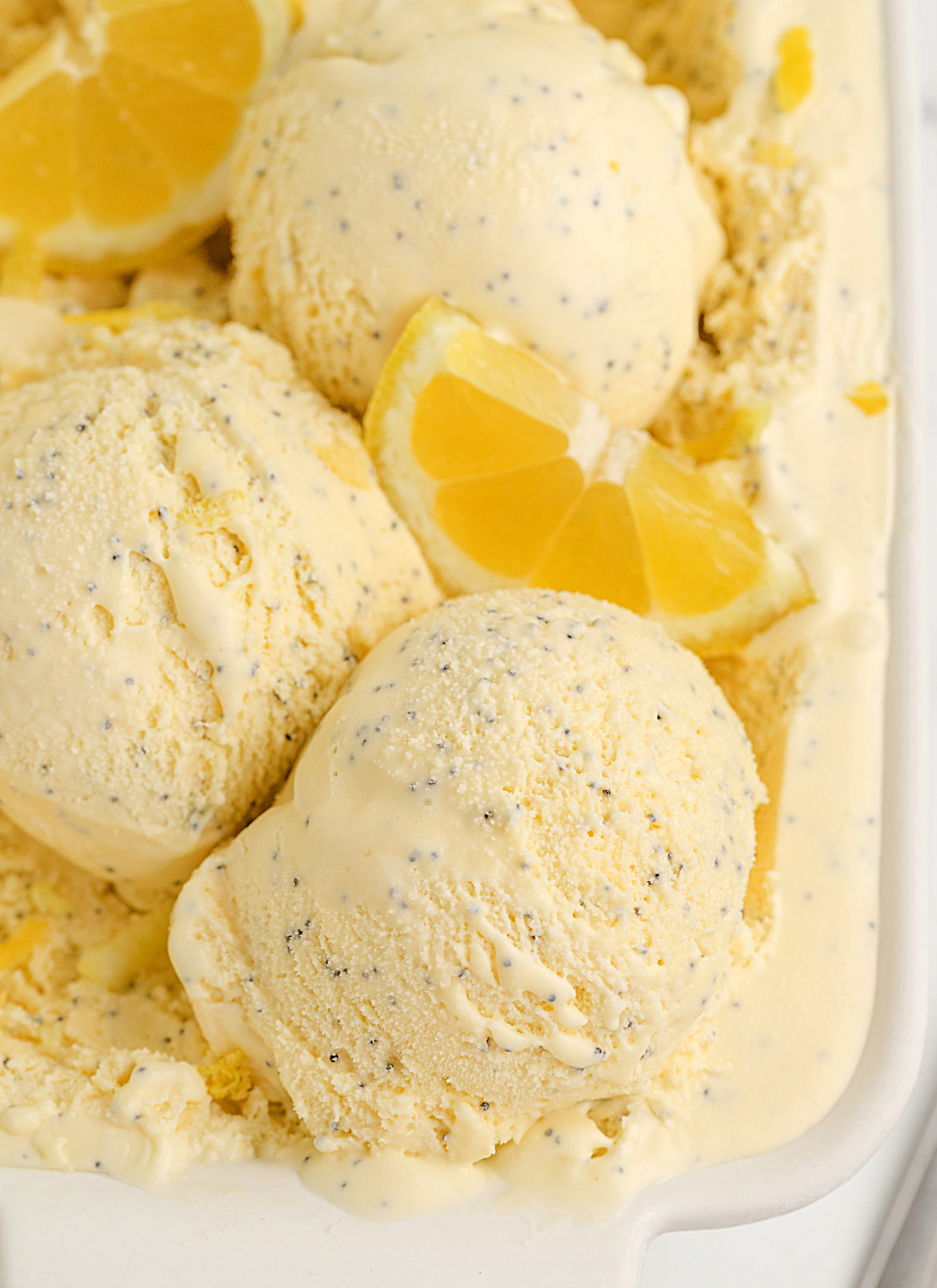 Creamy Lemon Poppy Seed Ice Cream with Buttermilk and Lemon Curd Close-up of scoops of creamy lemon poppy seed ice cream in a white dish with lemon wedges