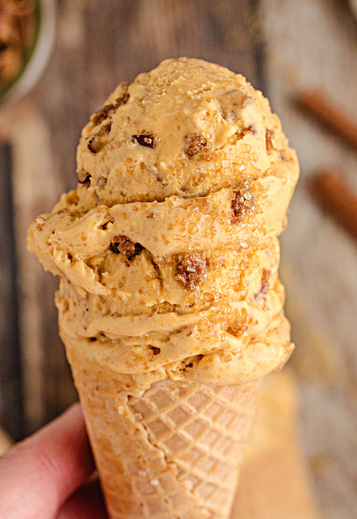 Tall scoop of Pumpkin Brown Sugar Crunch Ice Cream in a waffle cone, showing creamy pumpkin custard texture with brown sugar streusel pieces and turbinado sparkle.
