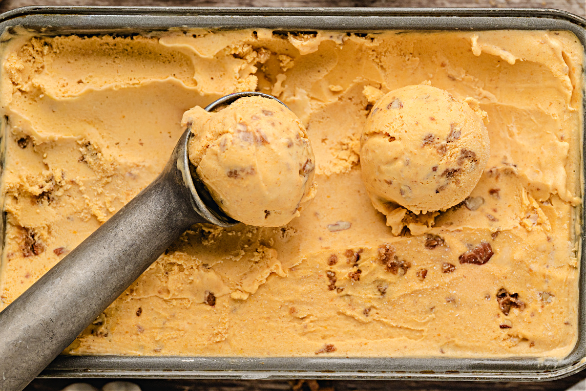 Pumpkin Brown Sugar Crunch Ice Cream by Noble Pig in a metal pan, showing creamy custard texture with baked pecan streusel folded through for a buttery crunch.
