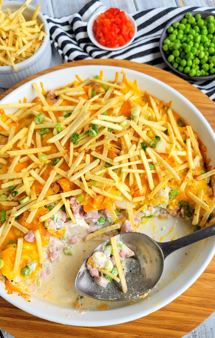 Top-down shot of the ham and cheese casserole with crunchy topping with a large spoon resting inside and half the casserole served.