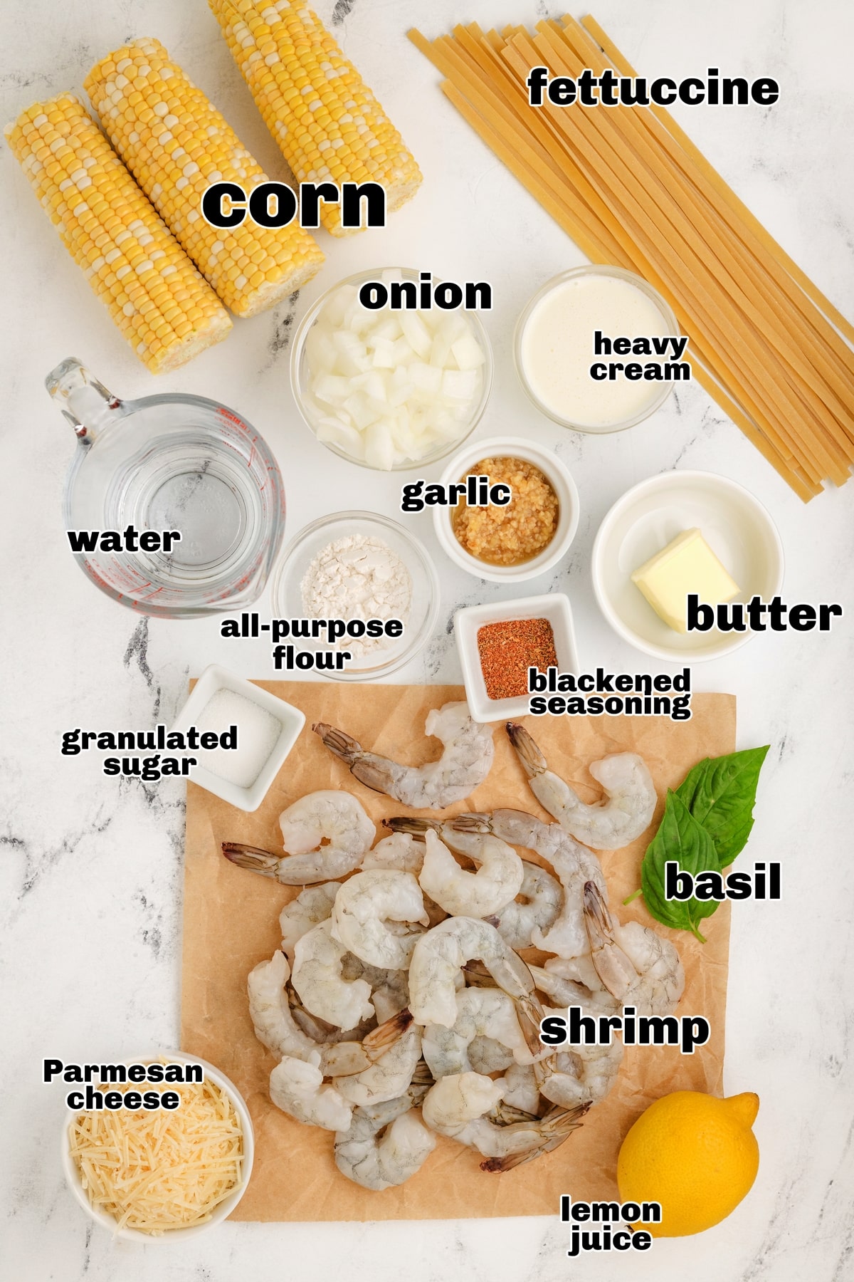 Ingredients for creamy corn and blackened shrimp pasta labeled on white surface.