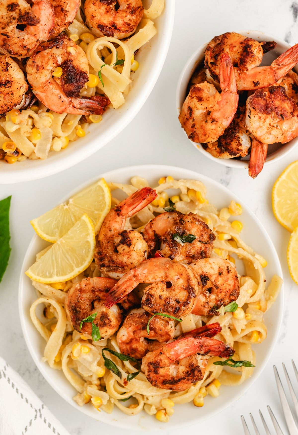 Bowls of creamy corn pasta topped with blackened shrimp and lemon wedges.